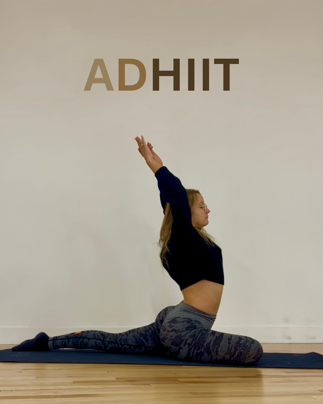 A woman practicing yoga on a mat, doing a backbend stretch with her arms raised above her head, in a room with wooden floors and a plain wall, with the word "ADHIT" overhead.