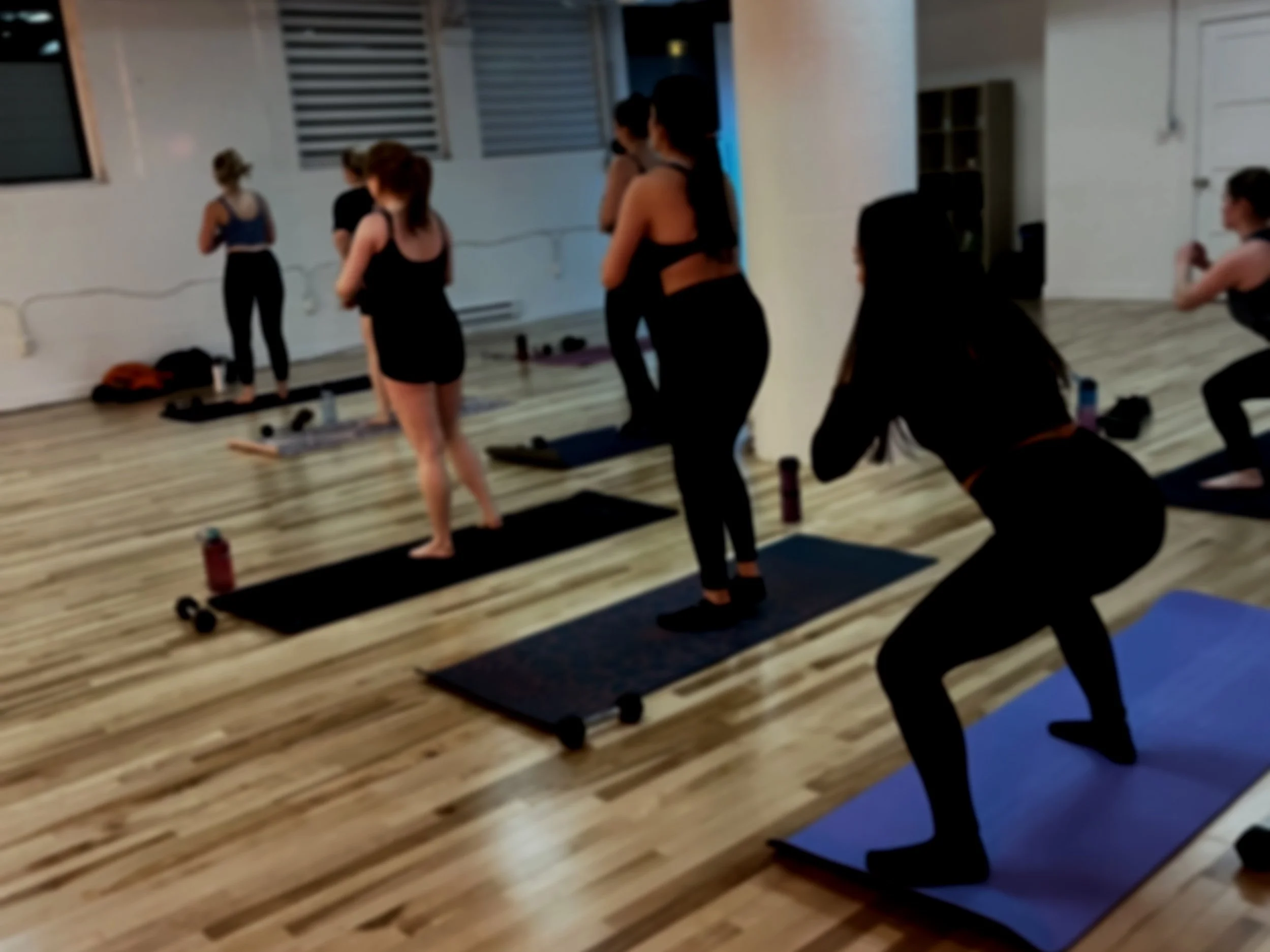 People attending a HIIT class in a studio, standing on yoga mats, facing the front of the room, with some seated and others standing.