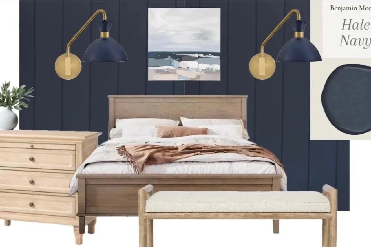 Bedroom with navy blue paneled walls, a wooden bed, matching nightstand, a bench at the foot of the bed, and two brass-arm wall lamps. A landscape painting hangs above the bed, and a white vase with green foliage is on the nightstand.