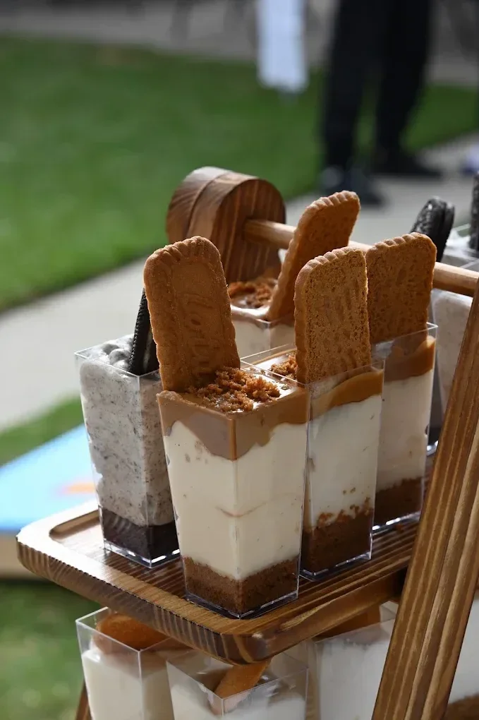 Three layered dessert parfaits in clear glasses topped with cookies, Oreo, and chocolate crumbles, arranged on a wooden tray