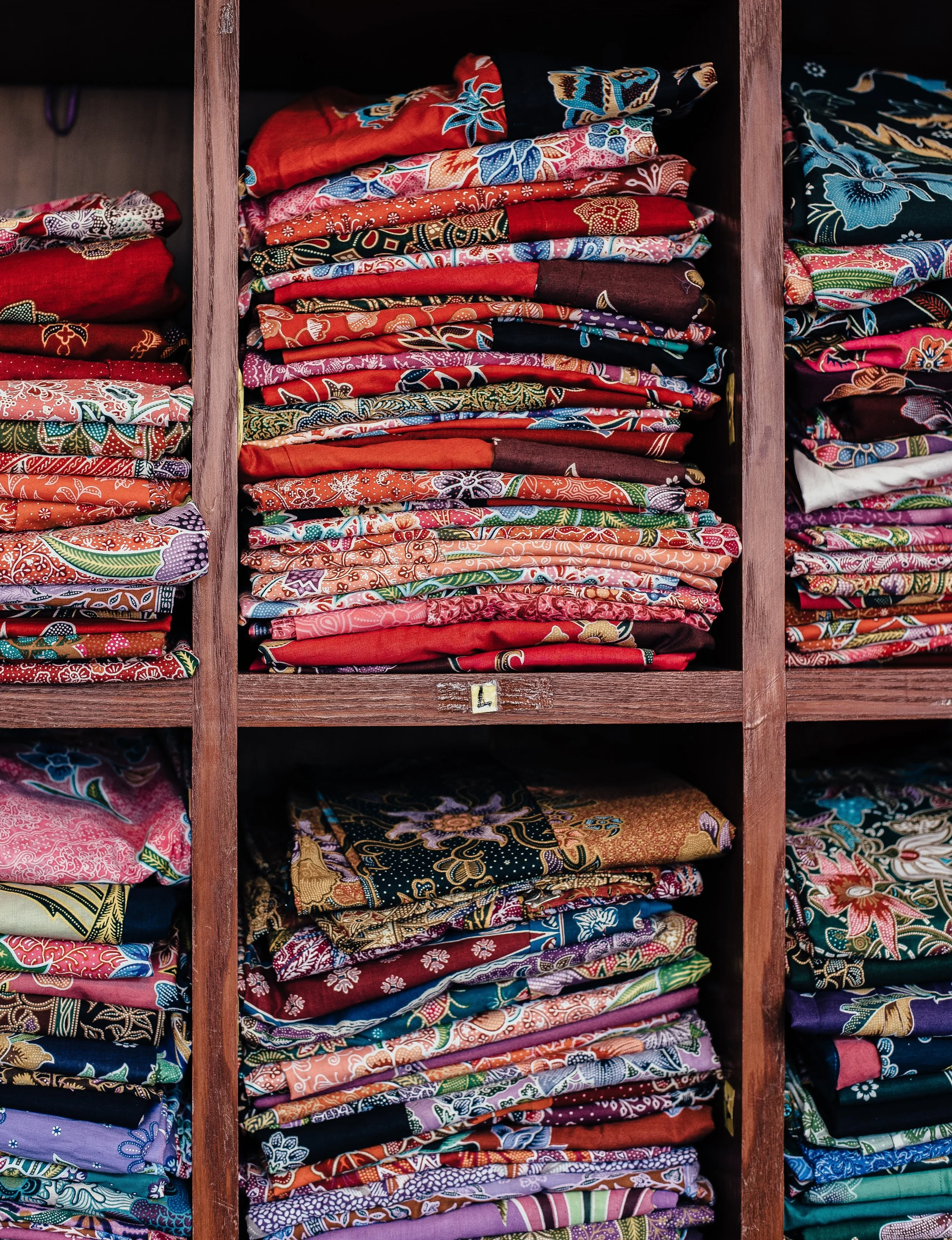 Stacks of colorful batik fabrics in wooden shelves