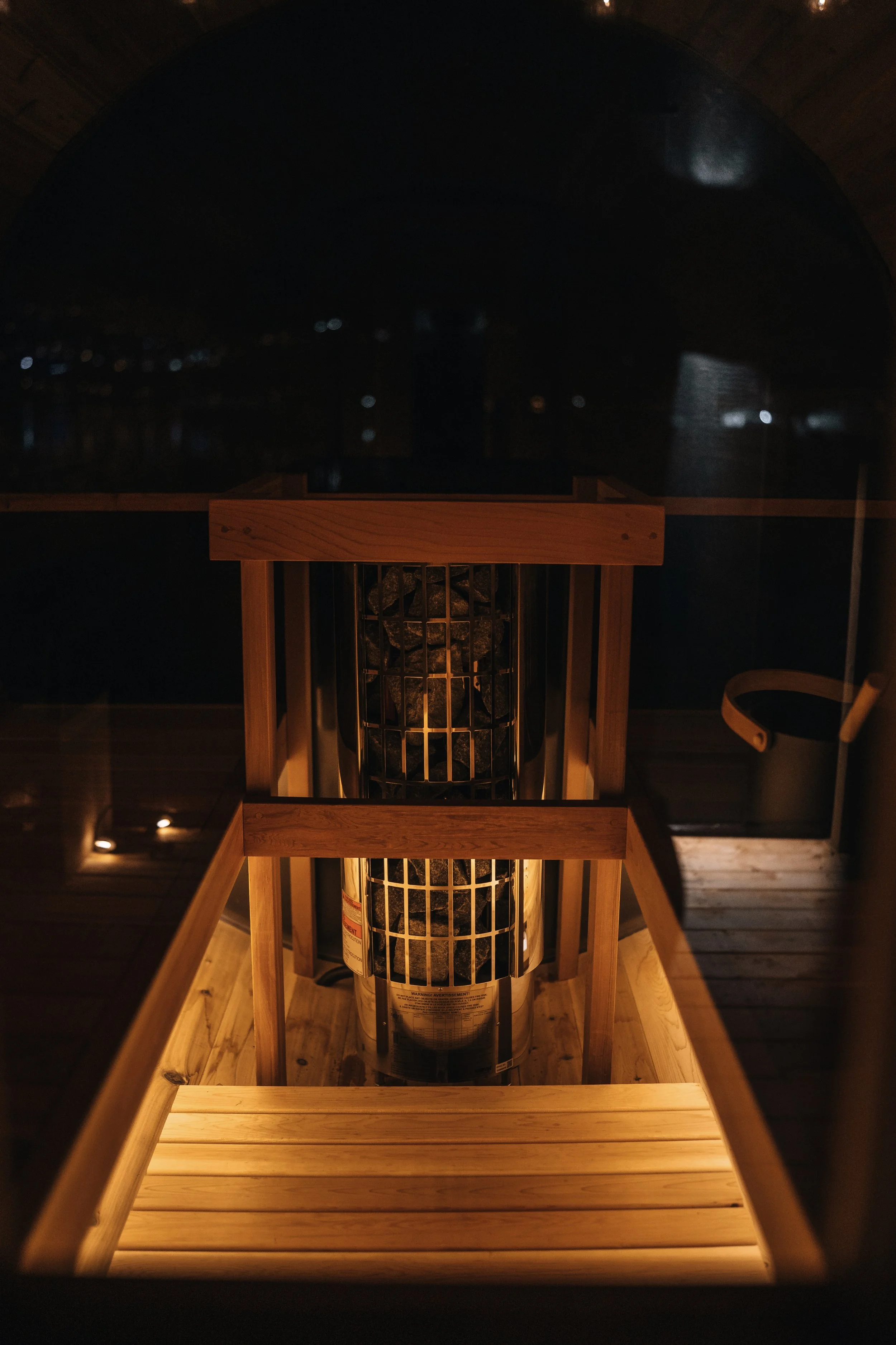 Inside a sauna with a wooden bench and a heater filled with rocks, viewed from above at night.