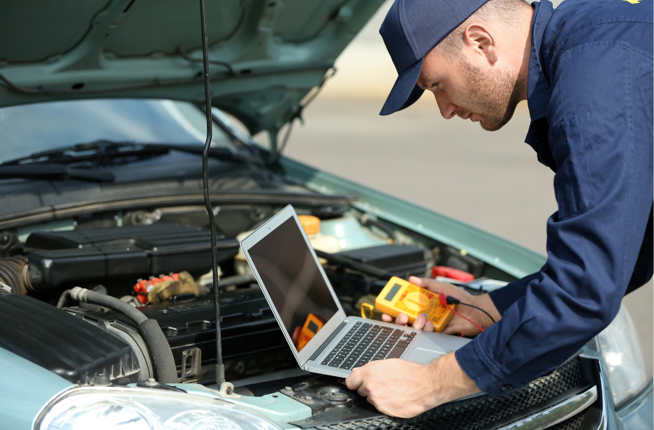 A mechanic using a multimeter and a laptop to diagnose a car engine with the hood open.