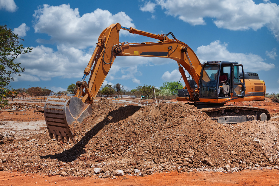 An orange excavator moving dirt on a construction site under a partly cloudy sky.