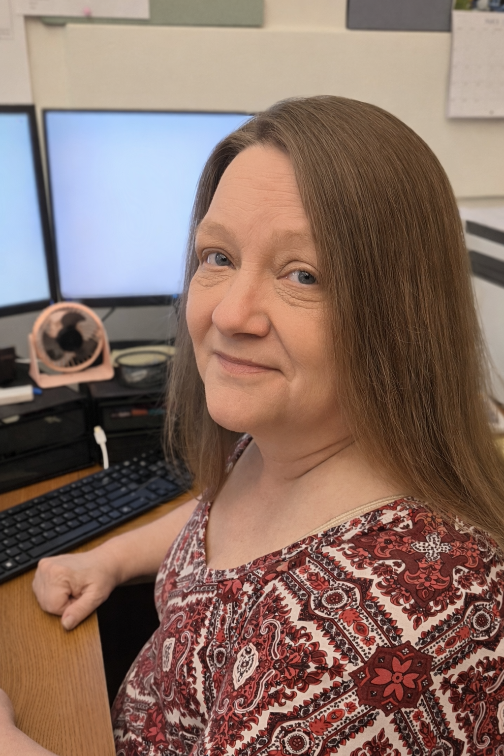 A smiling woman with glasses and hoop earrings inside a warmly lit room.