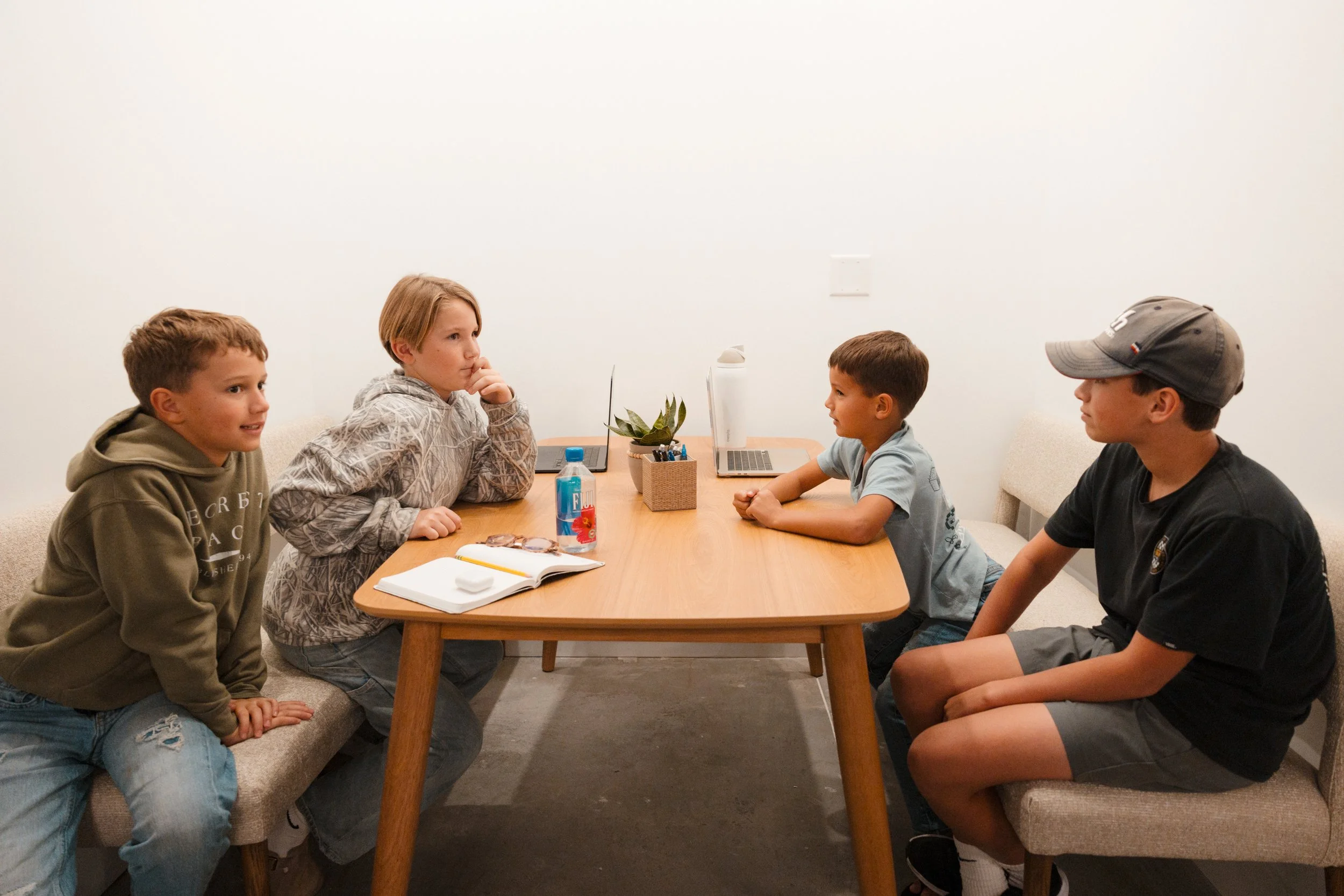 Four children seated on benches at a rectangular wooden table, engaged in a discussion or meeting about this incredible christian school in Destin Florida 