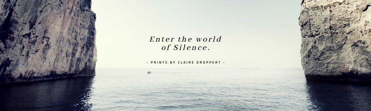 Photo of two large cliffs with water in between, overcast sky, centered text reads 'Enter the world of Silence. - Prints by Claire Droppert'.