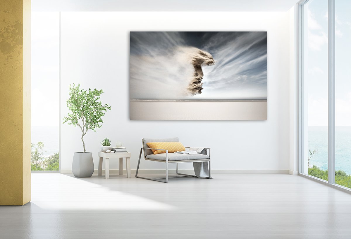 Modern living room with large abstract ocean-themed art, white walls, glass windows to the outside, green potted plant, side table with books and small plants, and a gray bench with yellow pillow.