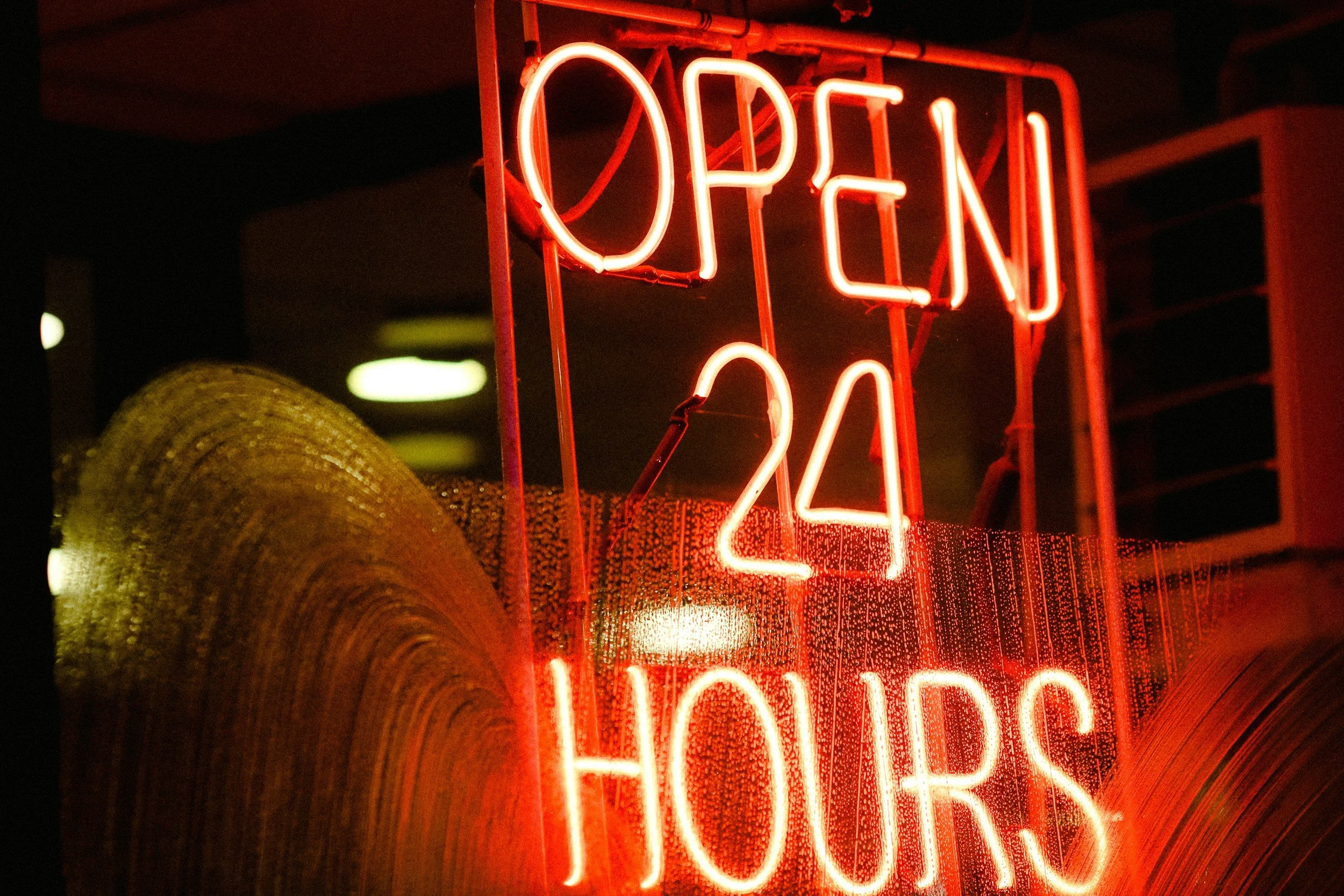 Rotes Neon-Schild mit der Aufschrift 'OPEN 24 HOURS' und Regentropfen auf der Scheibe