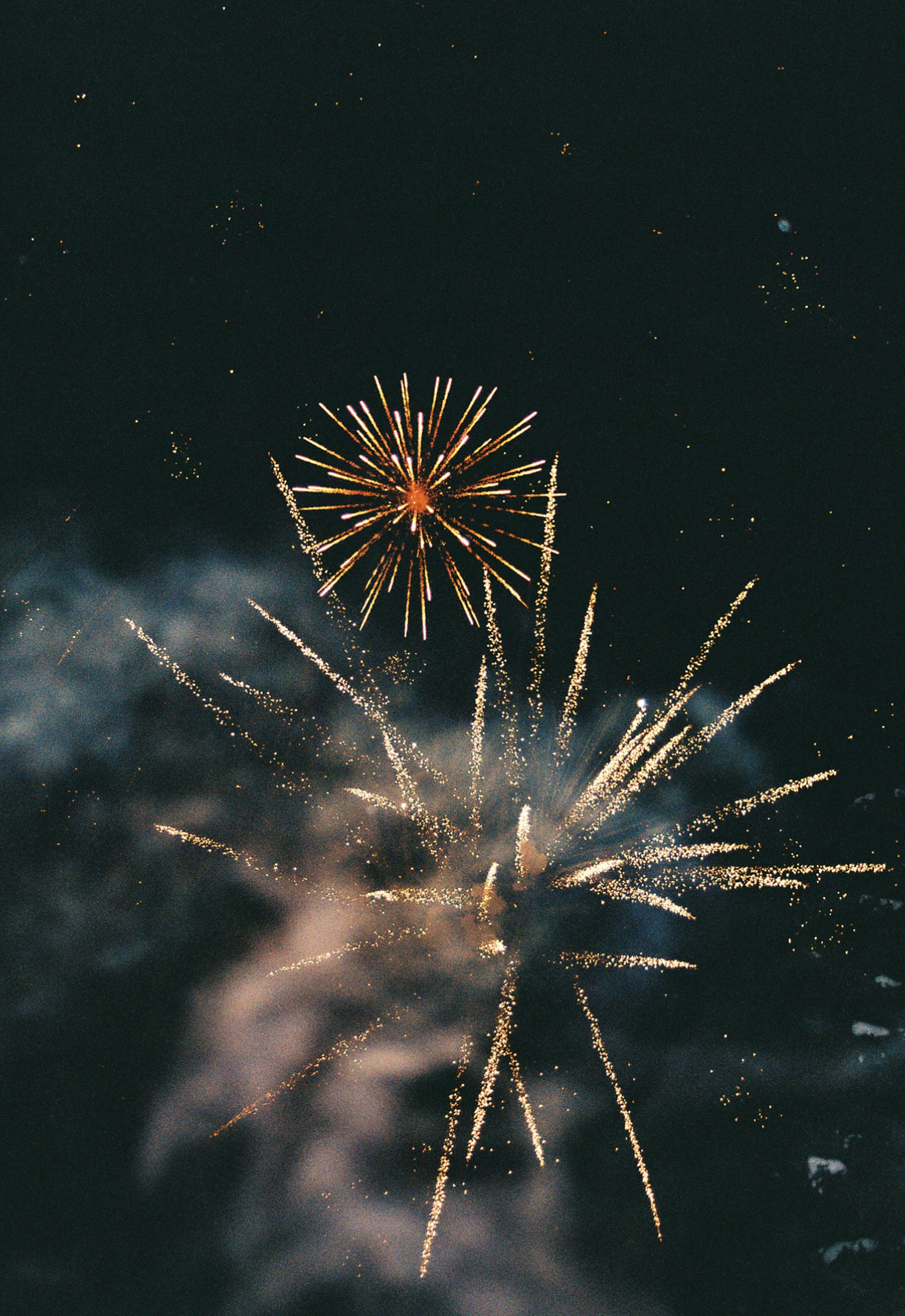 Bright fireworks burst in the night sky, displaying golden sparks and smoke trails. The festive atmosphere conveys joy and celebration.