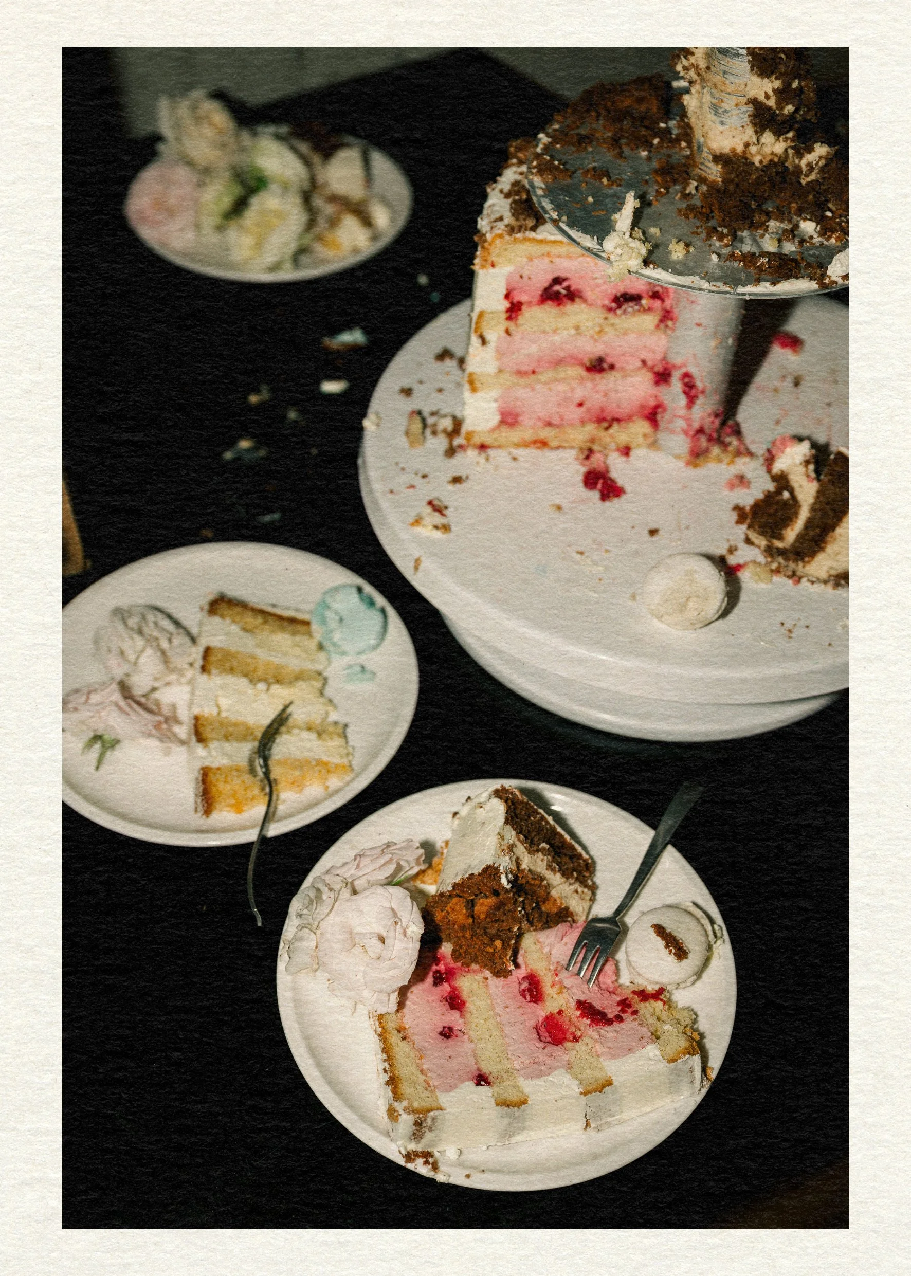A half-eaten cake with pink layers sits on a white stand. Two plates with slices and scattered crumbs accompany it, creating a messy, festive vibe.