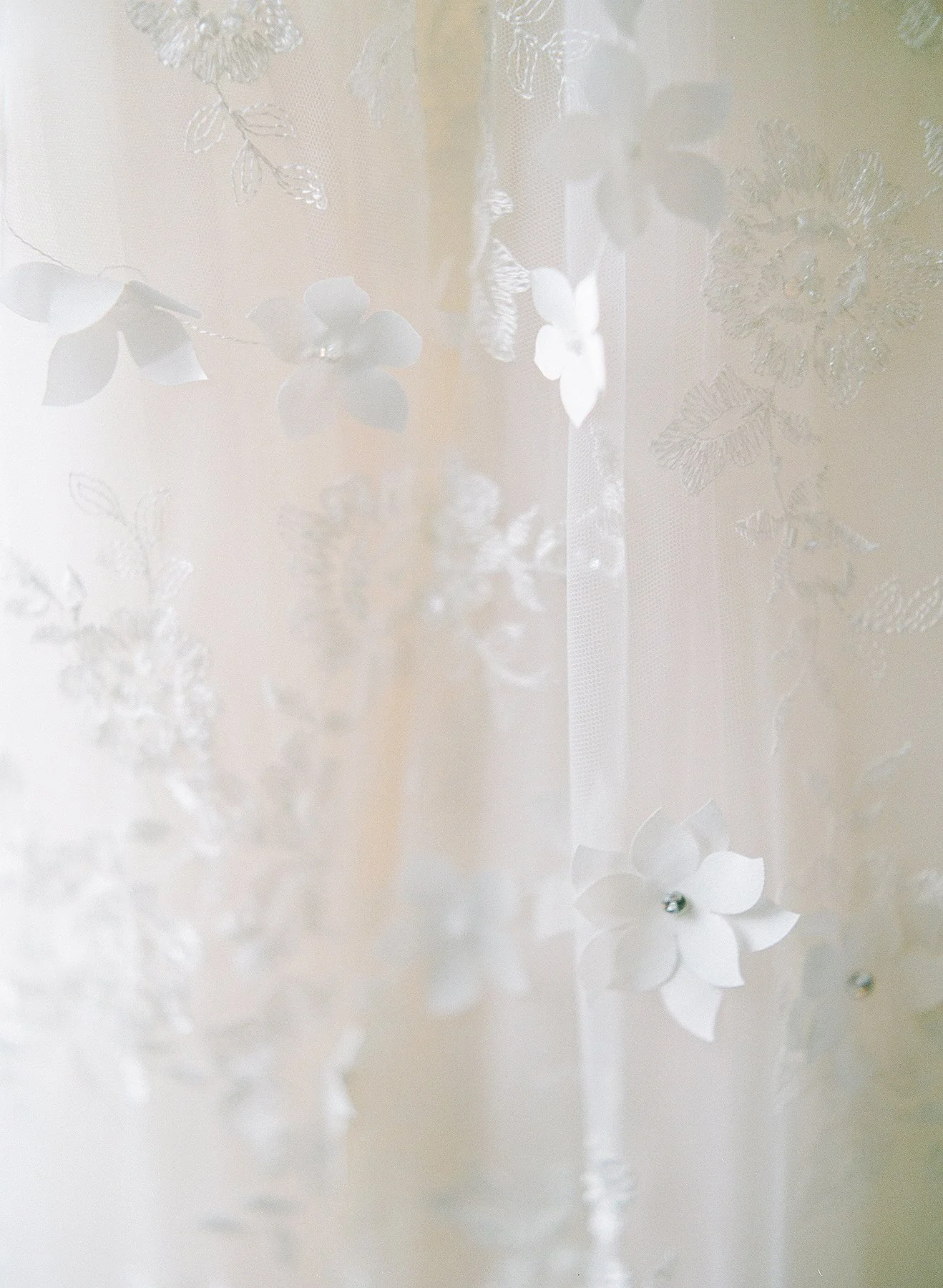 Delicate white lace veil adorned with floral patterns and 3D flowers, creating an elegant and ethereal visual with a soft focus.