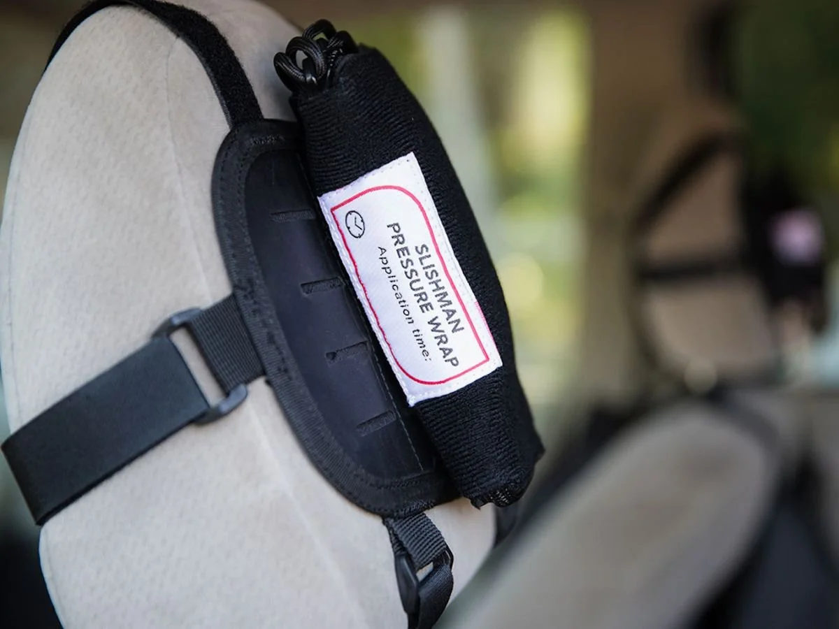 Close-up of a bicycle saddle with a black strap that holds a slip-on pressure wrap labeled 'SLUSHMAN PRESSURE WRAP APPLICATION TIME' in red and black text.