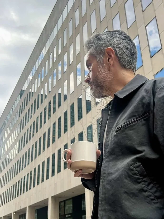 Creative director Synden Hope-Johnston holding a coffee outside a modern office building.