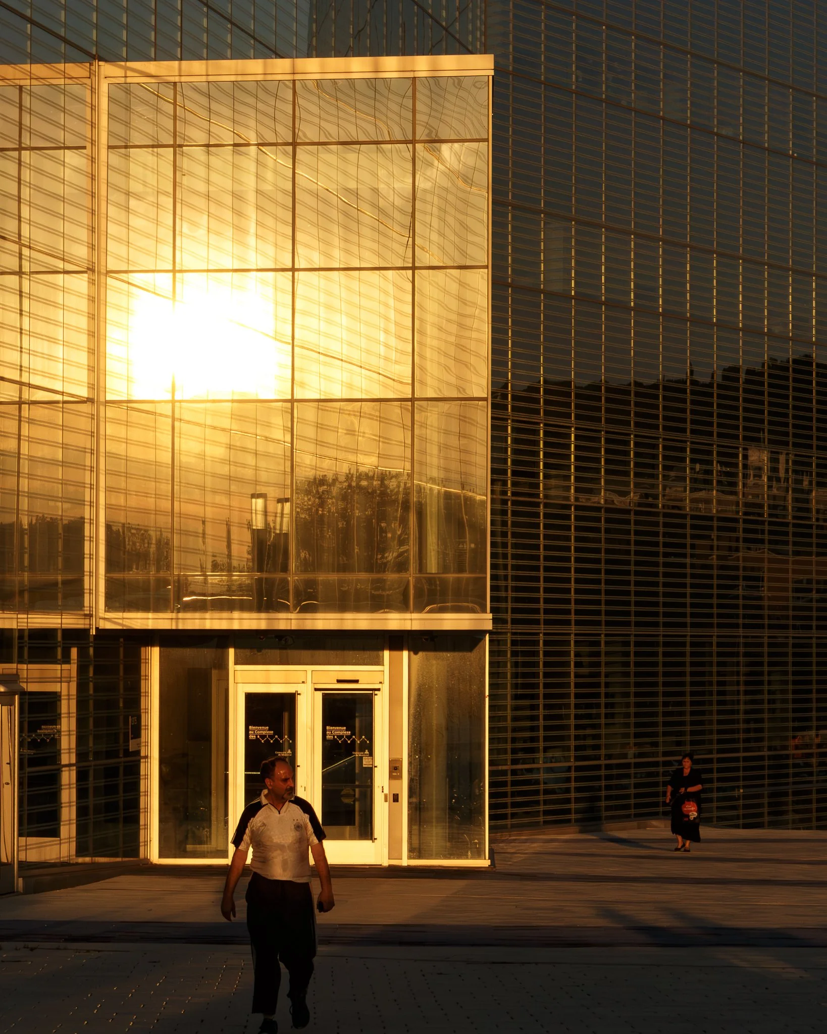 Sun reflecting off a glass building with two people walking outside.