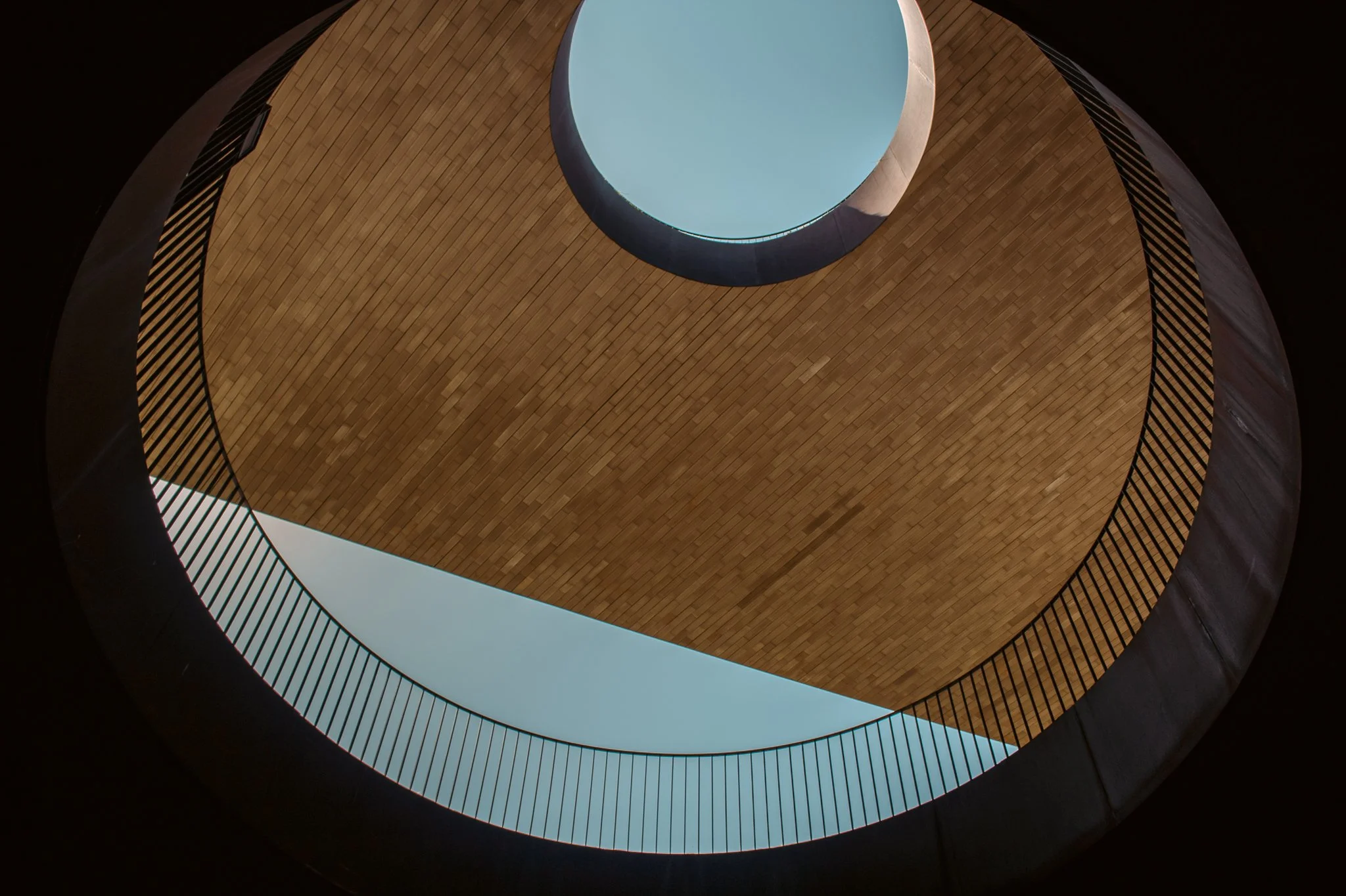 Interior view of a spiral staircase with wooden steps, black railings, and a circular skylight at the top.