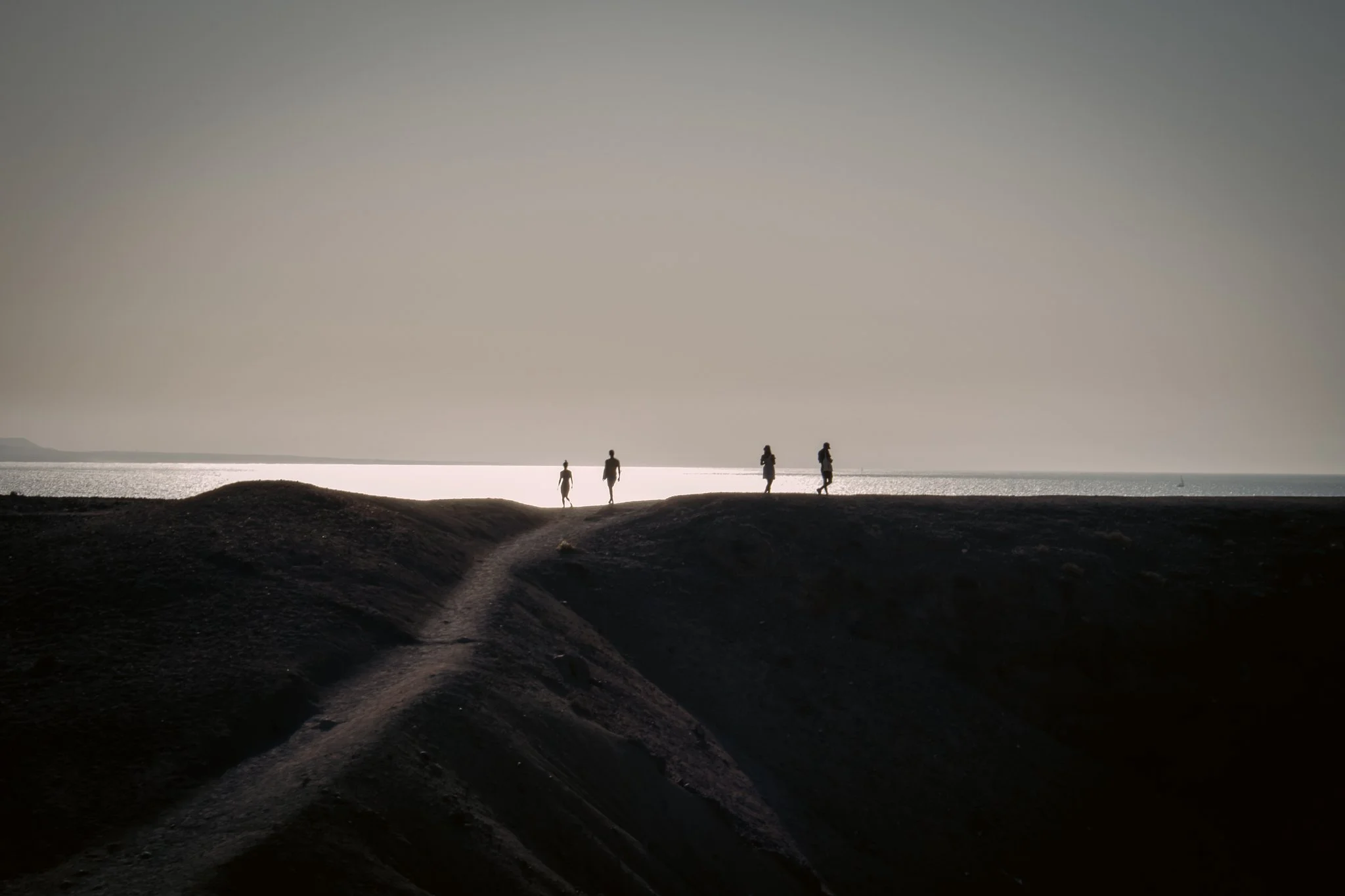 Silhouettes of five people walking along a hilltop near the ocean during sunset or sunrise.