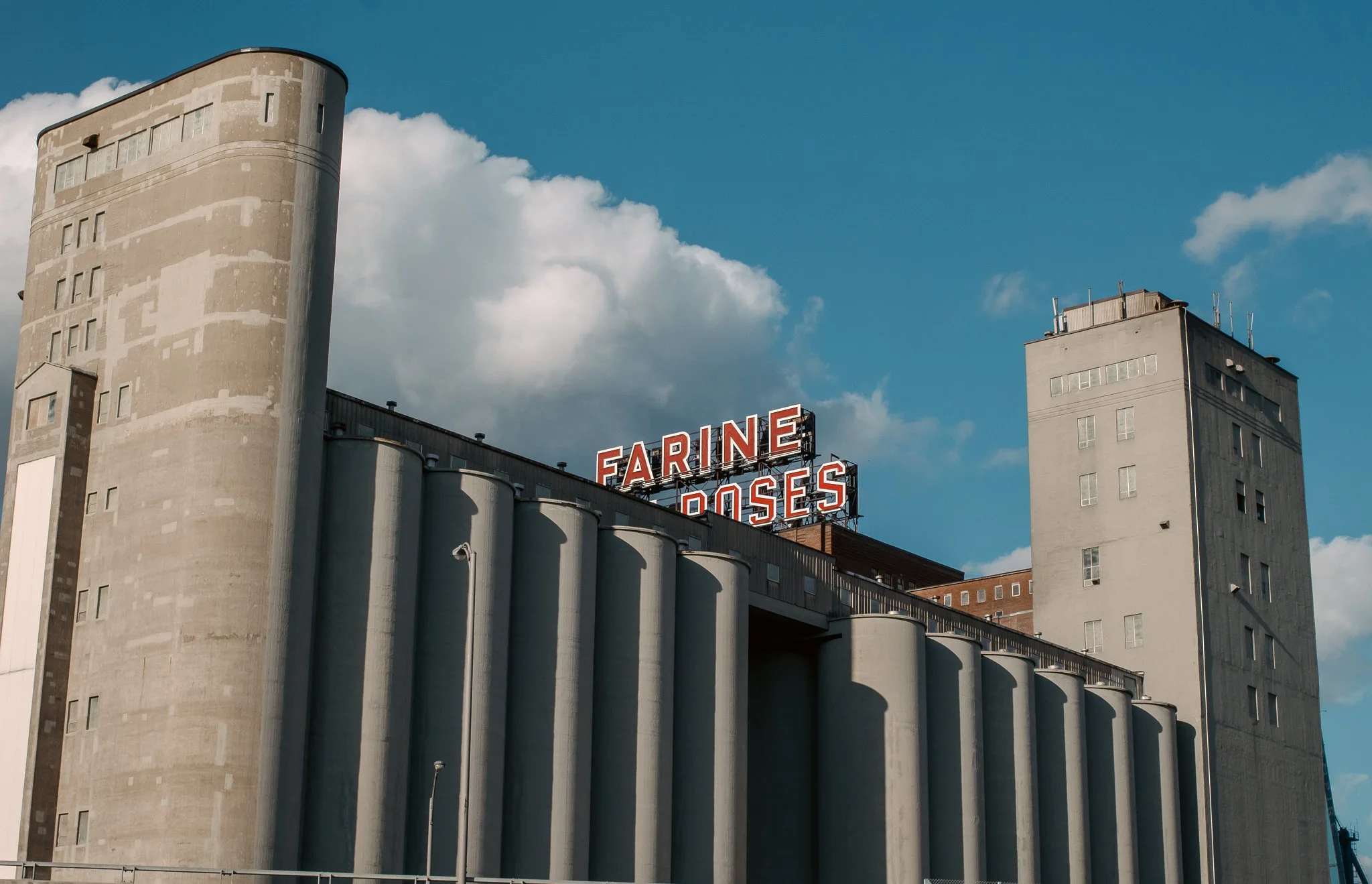 An industrial building with silos and a sign that reads "FARINE ROSES" in red letters on top.