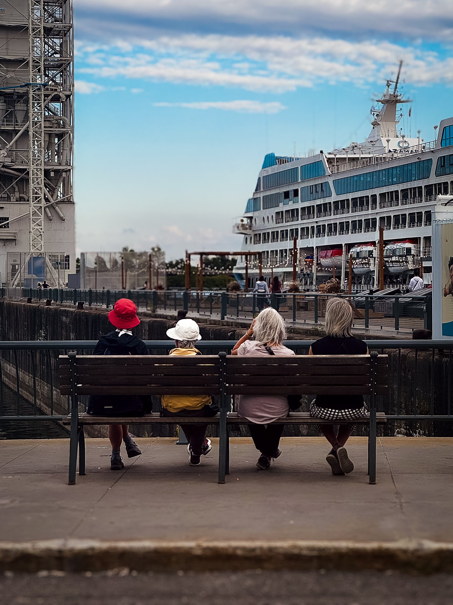Four people sitting on a bench overlooking a dock with a large cruise ship in the background.