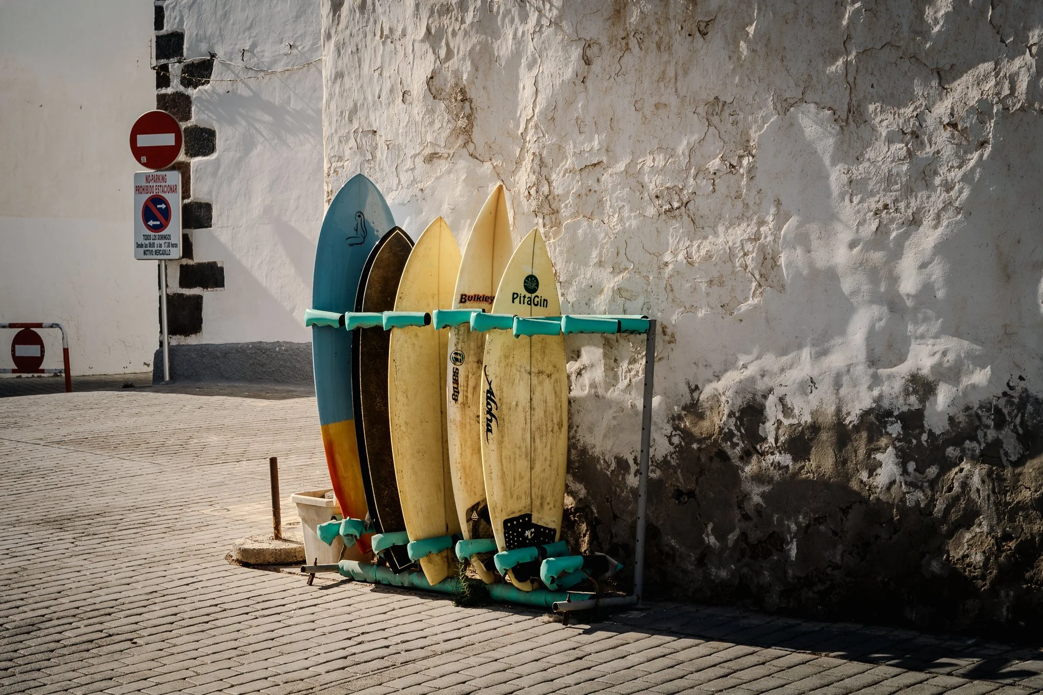 A rack of colorful surfboards leaning against a textured white wall in a sunny outdoor area.