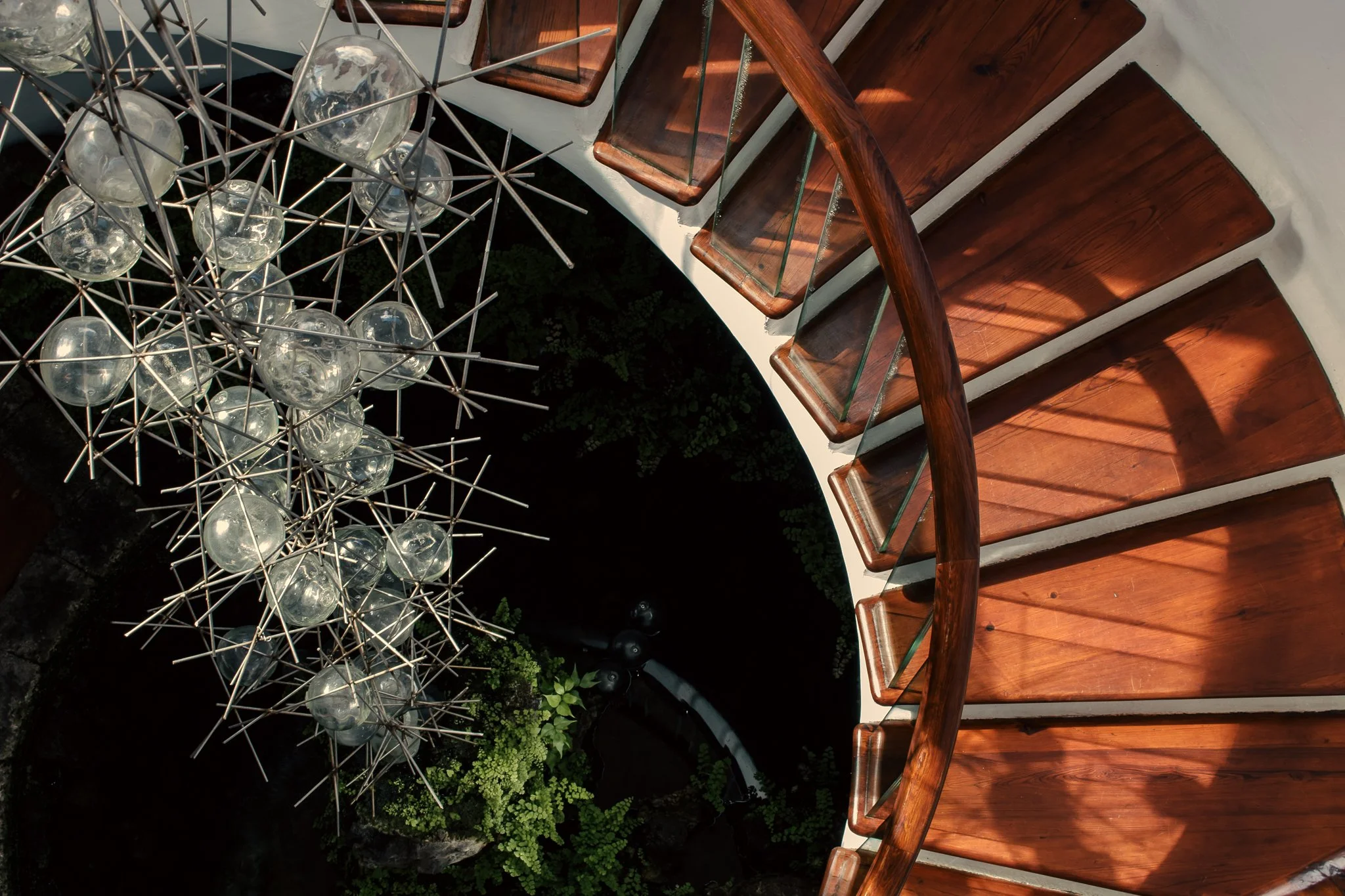 View of a spiral staircase made of wood and glass, with a modern hanging light fixture with glass globes visible from above.