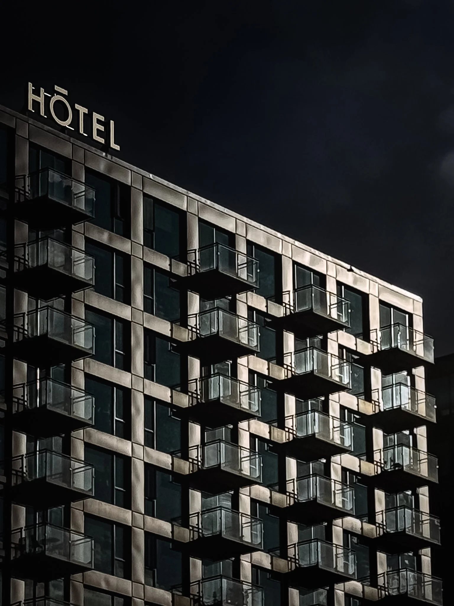 Night view of a modern hotel building with numerous glass balconies and a sign that reads 'HOTEL' at the top.