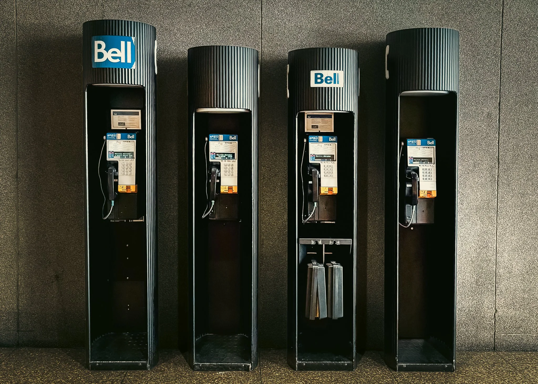 Four empty black phone booths with Bell branding against a plain wall.