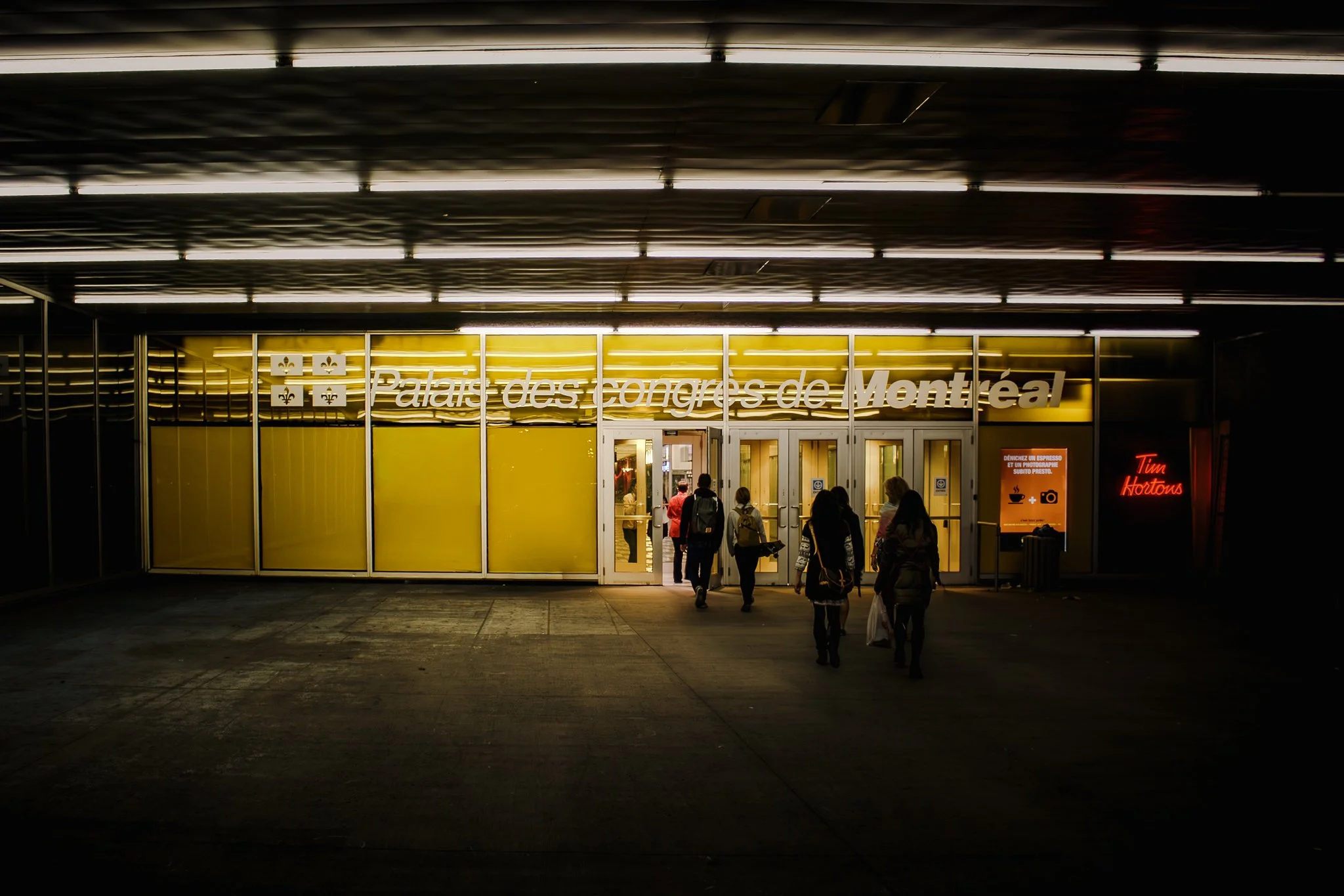 People walking into the Montreal Convention Center at night, with illuminated signage in French and a red Tim Hortons sign nearby.