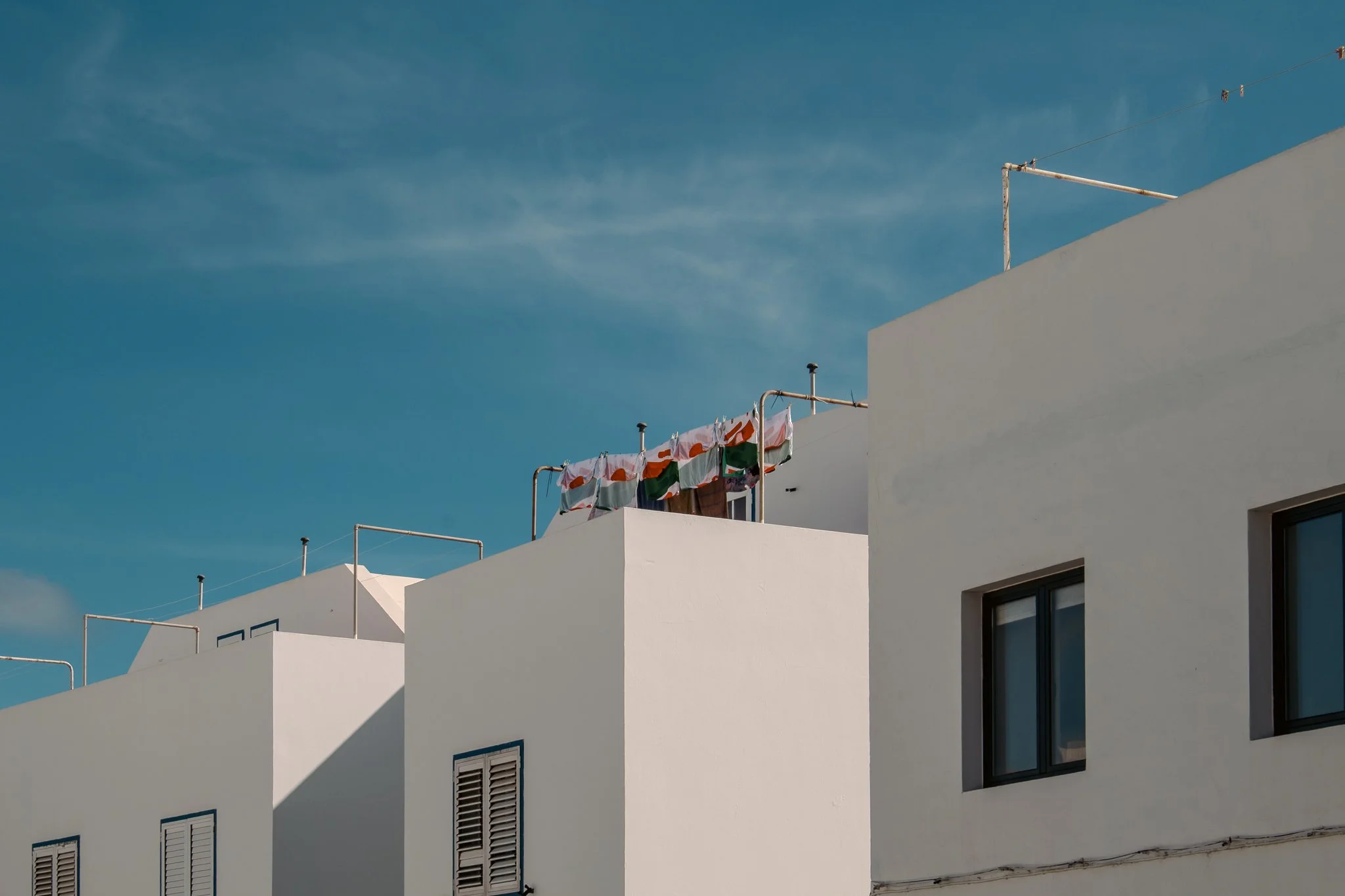 White modern buildings with windows under a blue sky, laundry hanging on lines on the rooftop.