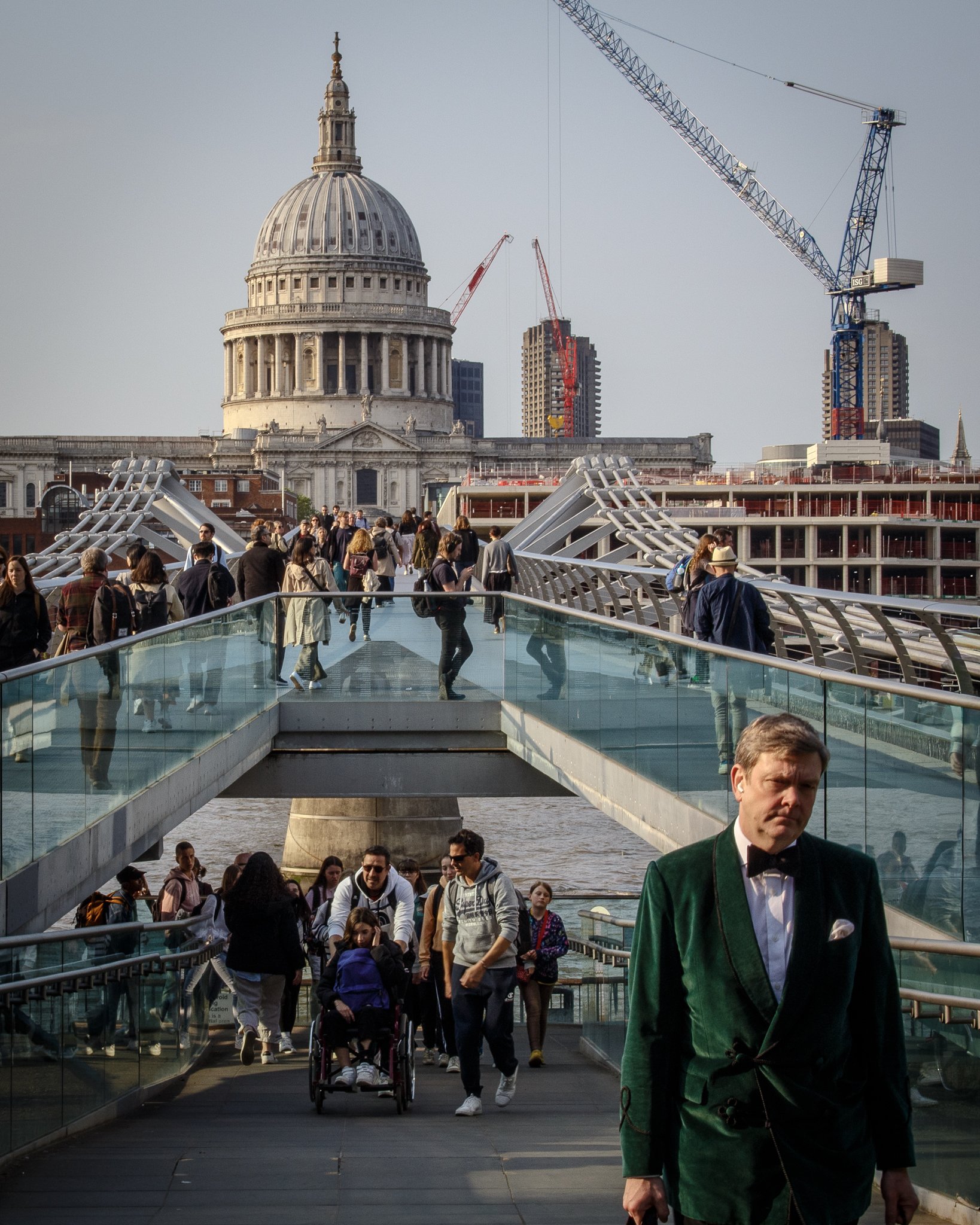 People walking on Millennium Bridge with St. Paul's Cathedral in London in the background, construction cranes in the cityscape.