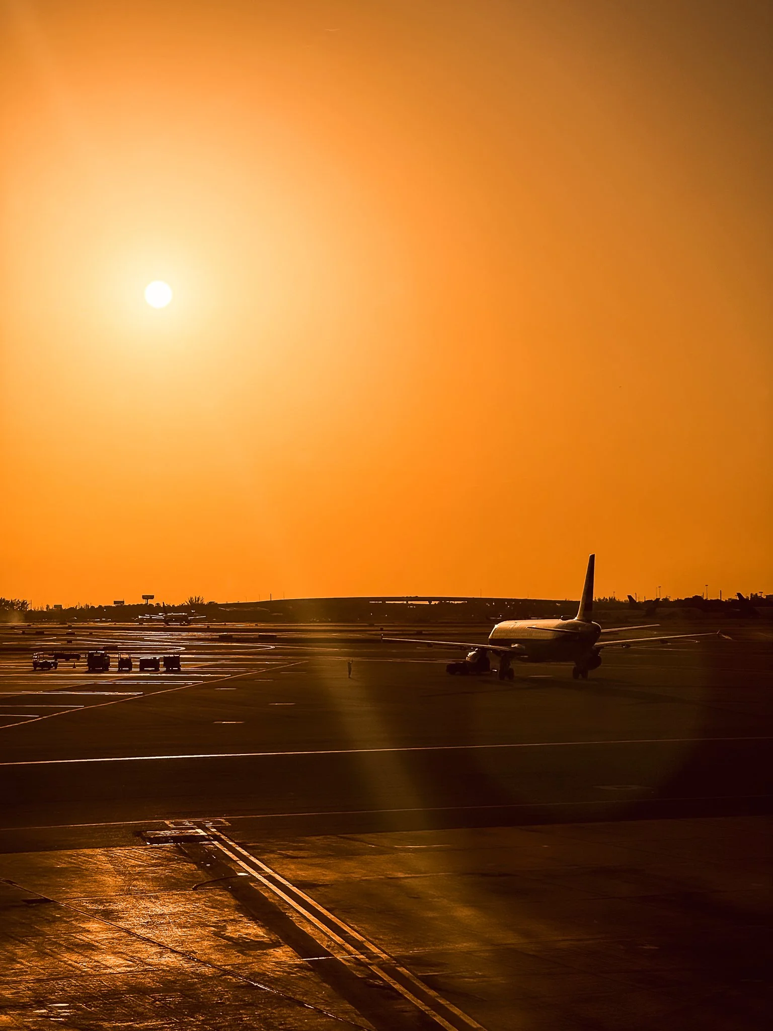 An airplane on the tarmac at sunset with the sun low in the sky and an orange hue in the atmosphere.