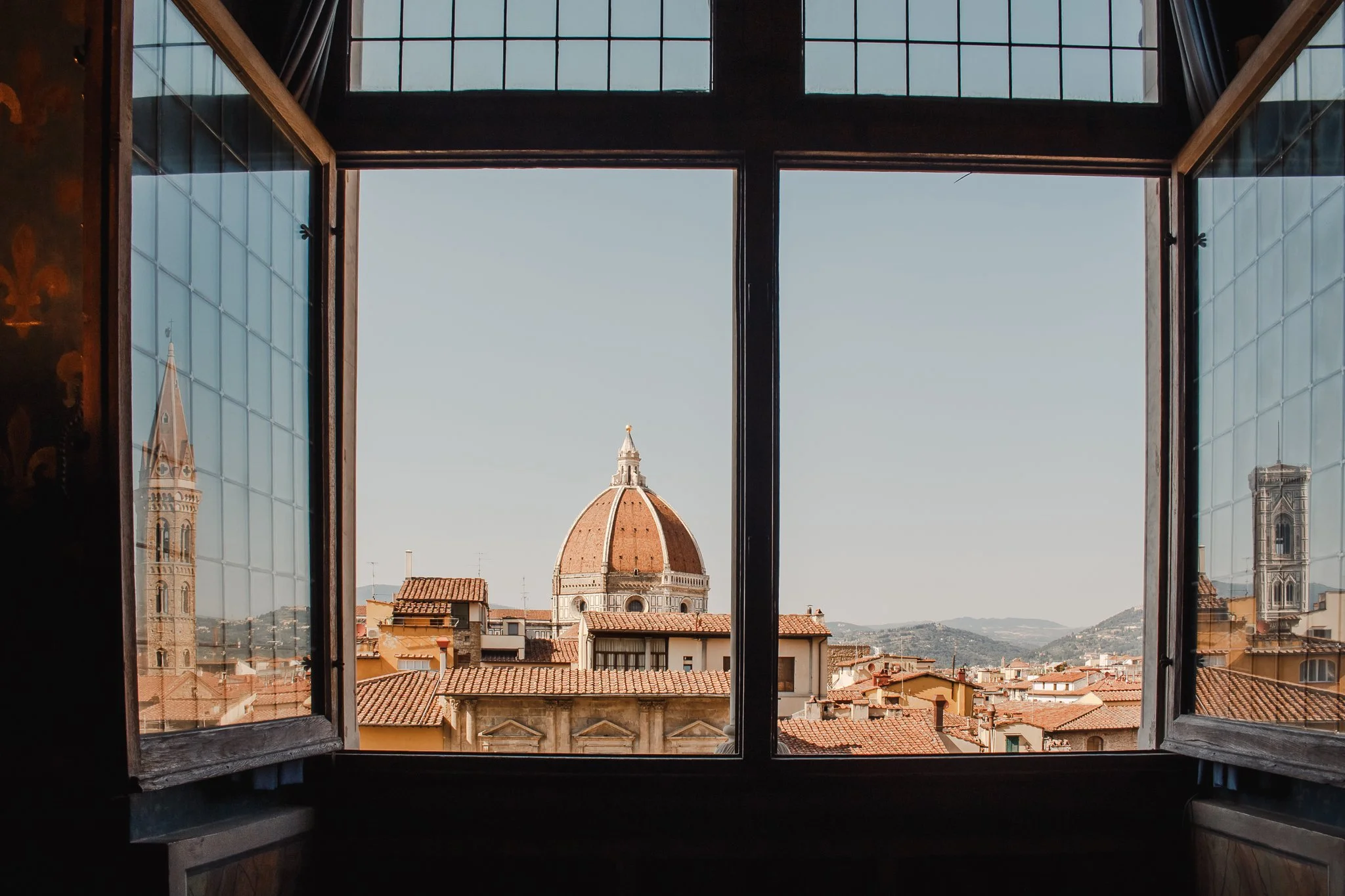 View of Florence, Italy through an open window, featuring the Florence Cathedral's dome and surrounding rooftops.
