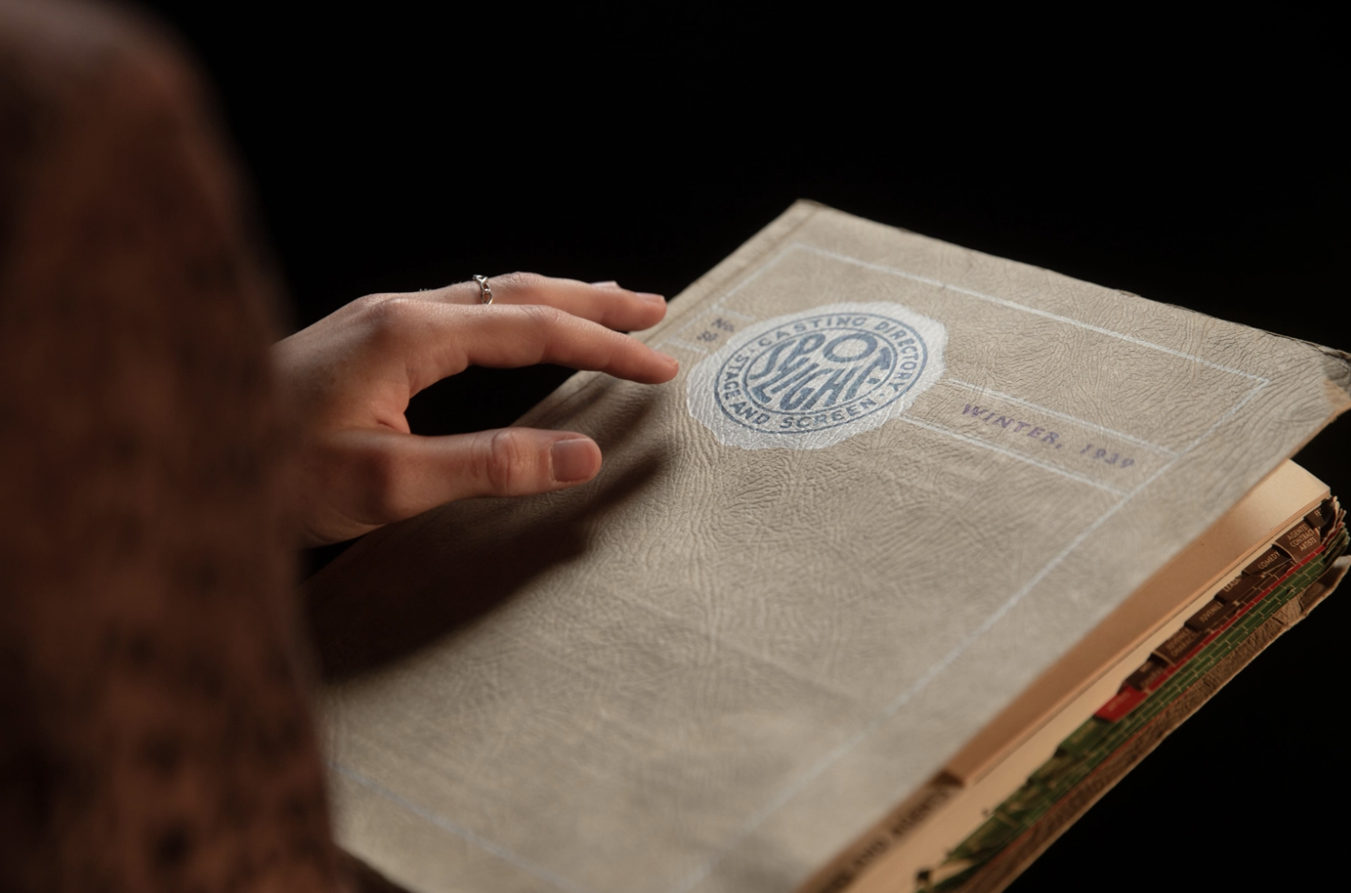 Close-up of a person's hand holding an old, worn notebook or scrapbook with a vintage logo reading 'Speed Light' on the cover, and a handwritten note 'Winter 1970'.