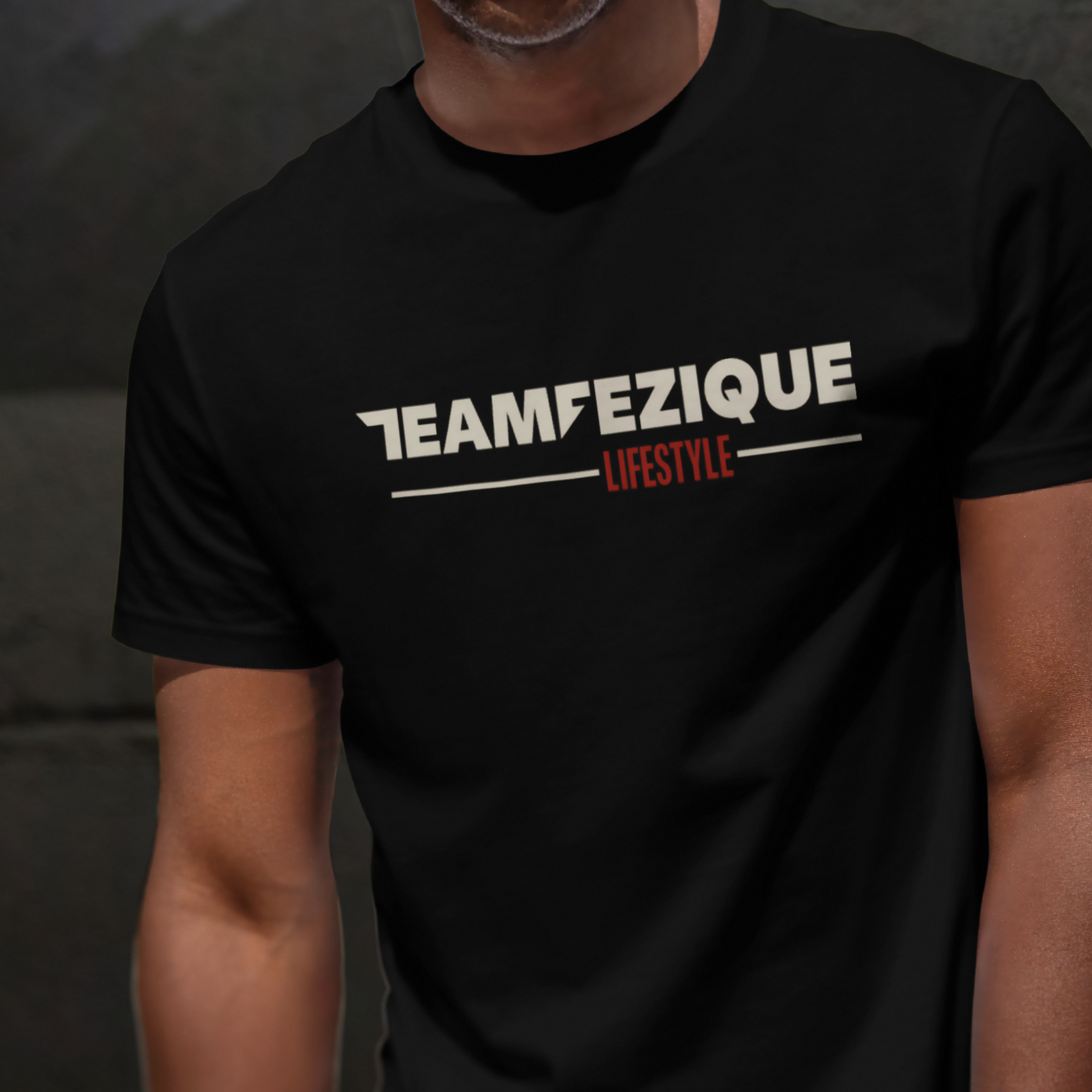 A person wearing a black T-shirt with the text 'TEAM FEZIQUE LIFESTYLE' in white and red letters.