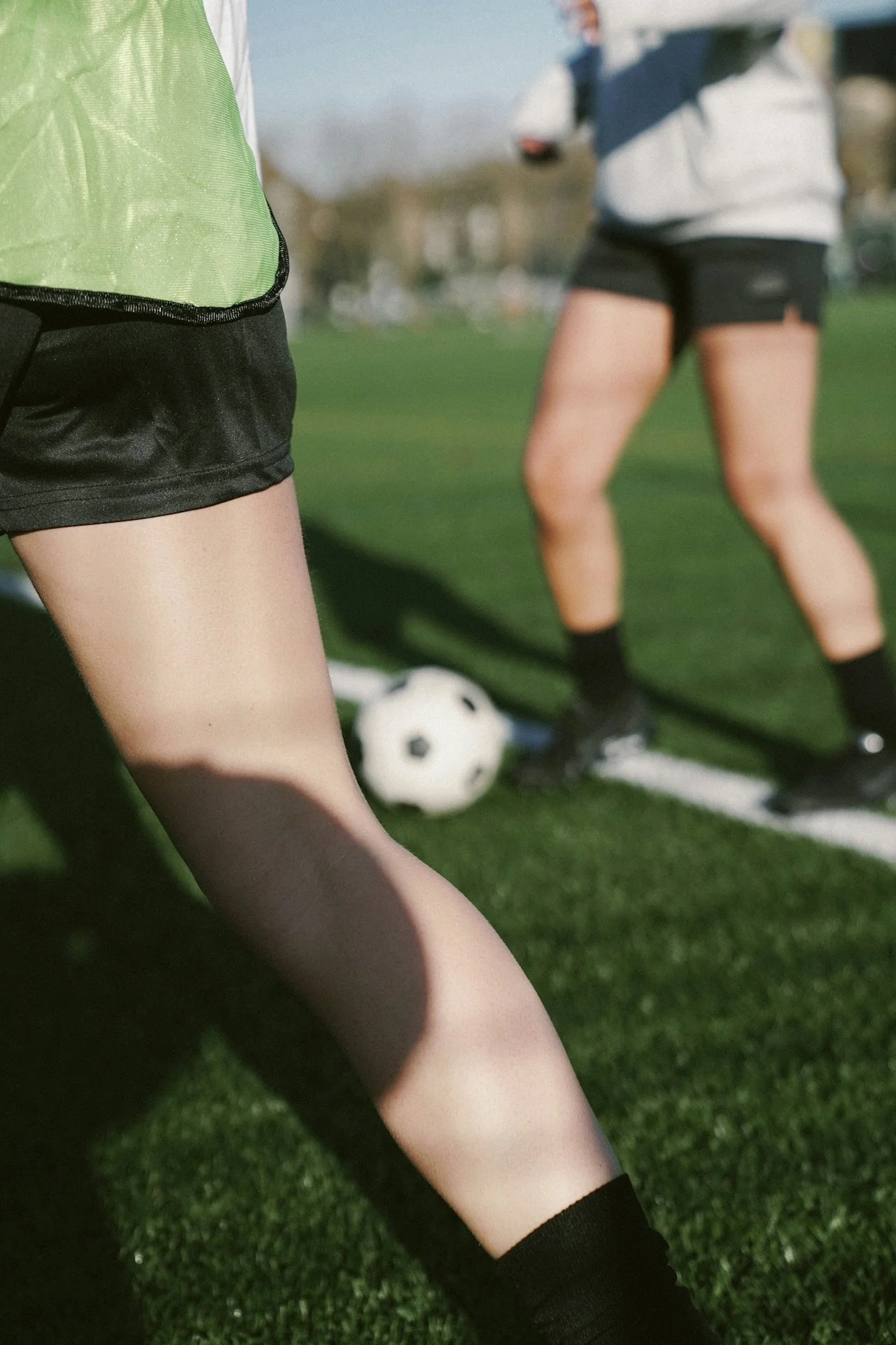 Close-up of two people wearing soccer uniforms on a field with a soccer ball between them.