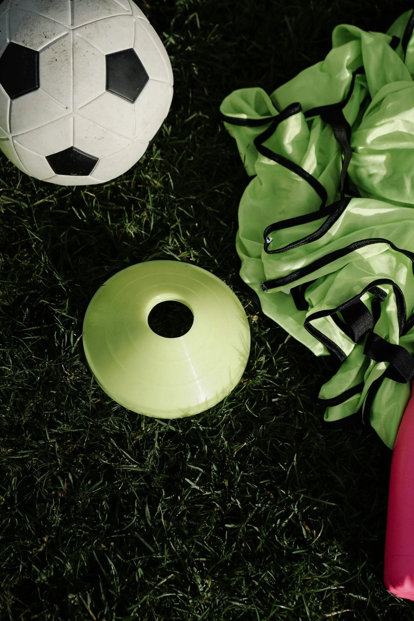 A soccer ball, a spinning disc, a neon green jacket, and a pink water bottle on grass.
