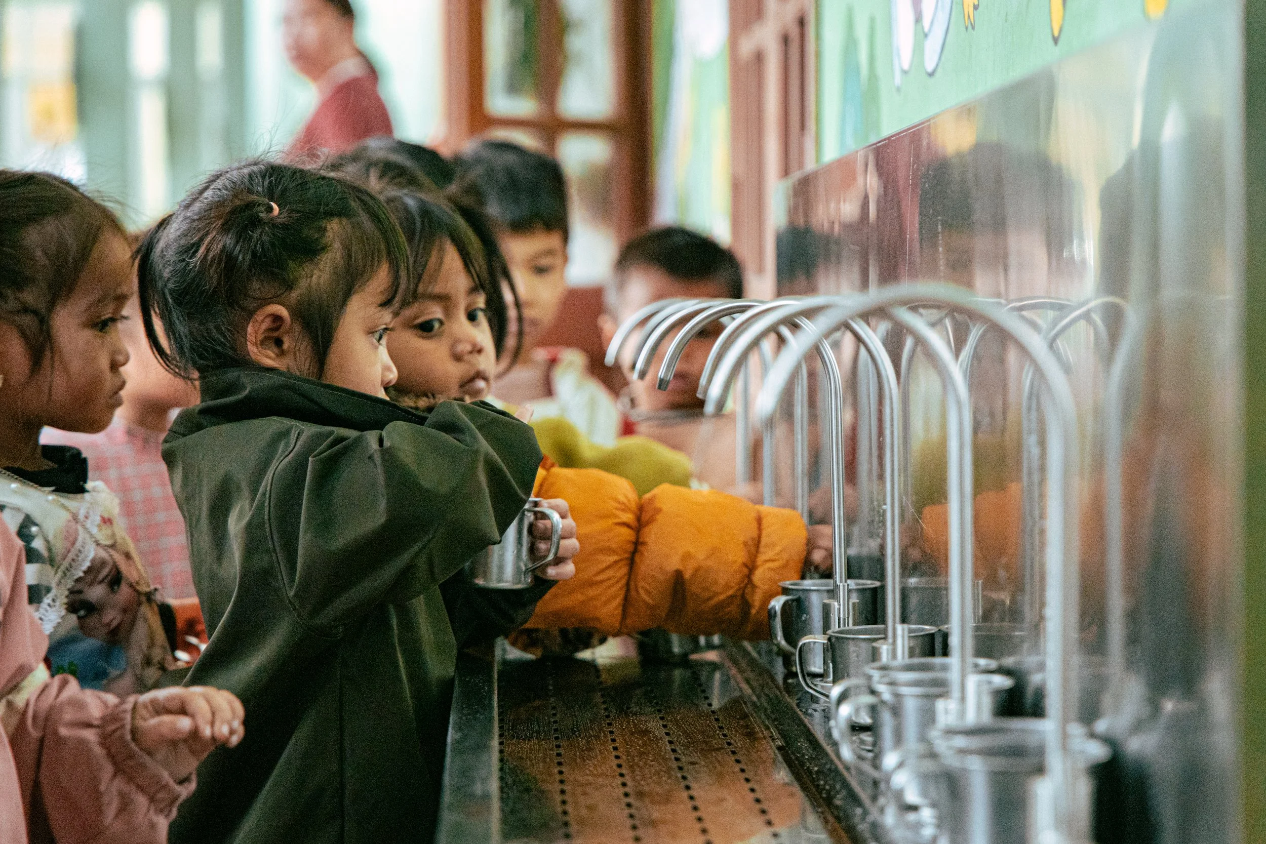 Children using a filtered water fountain in a school hallway.