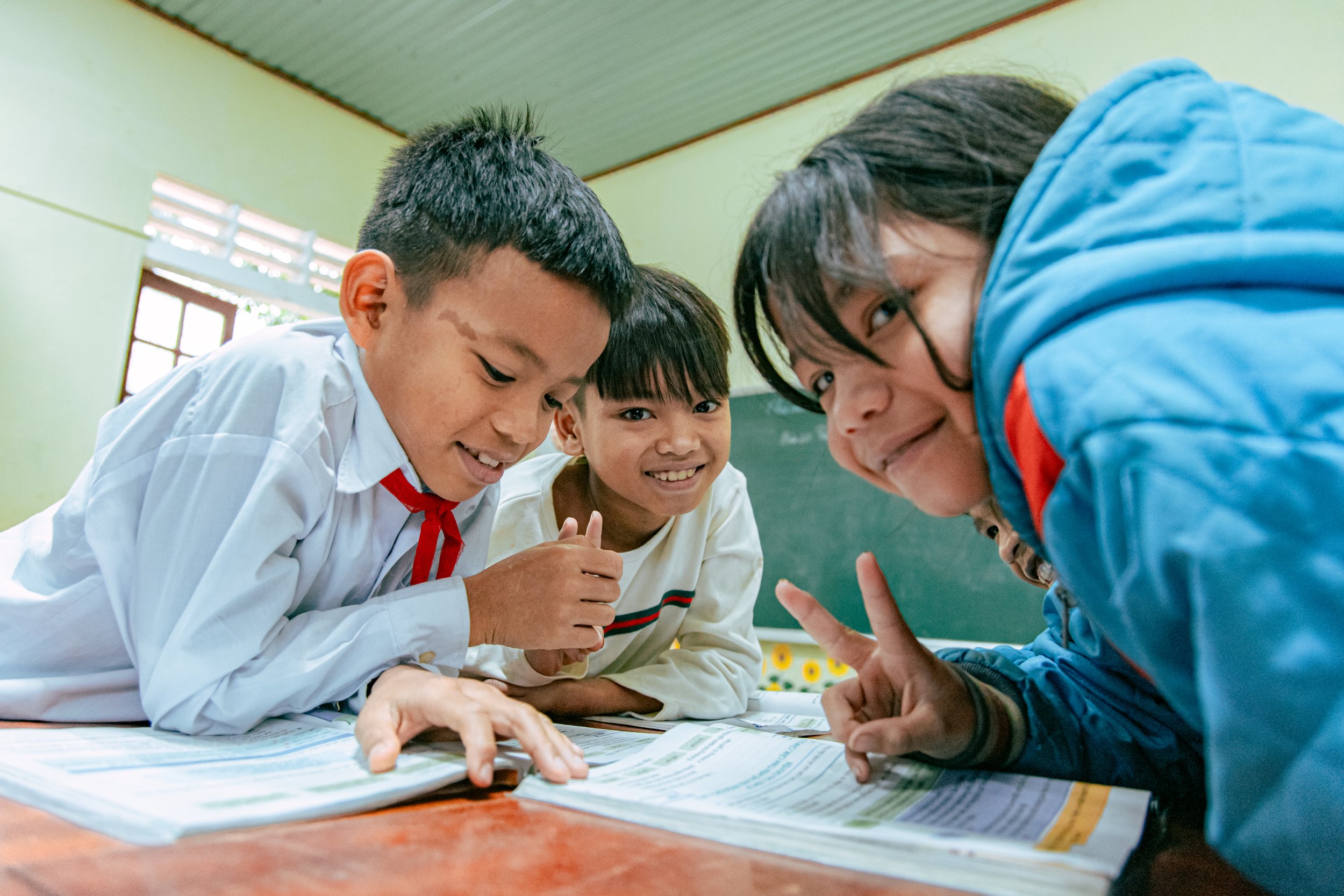 A group of children are gathered around a table looking at papers, engaging in a discussion in a classroom.