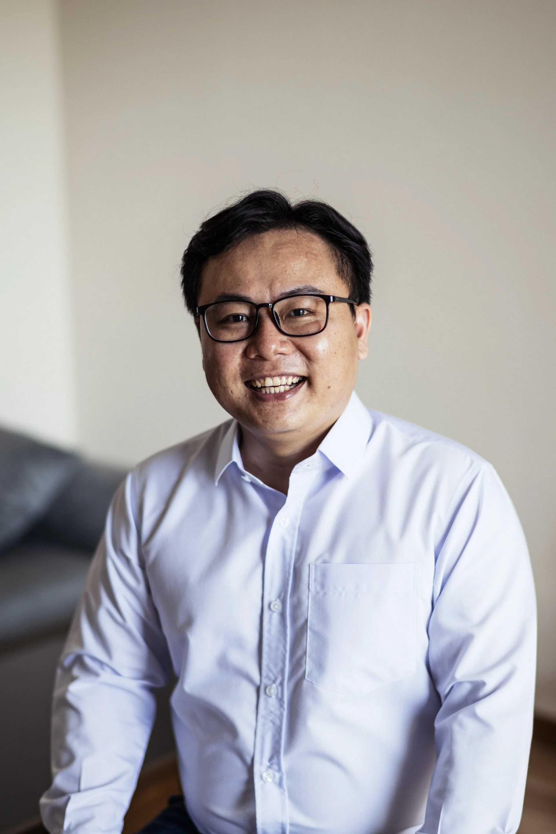 A man with glasses and dark hair, smiling, wearing a white dress shirt.