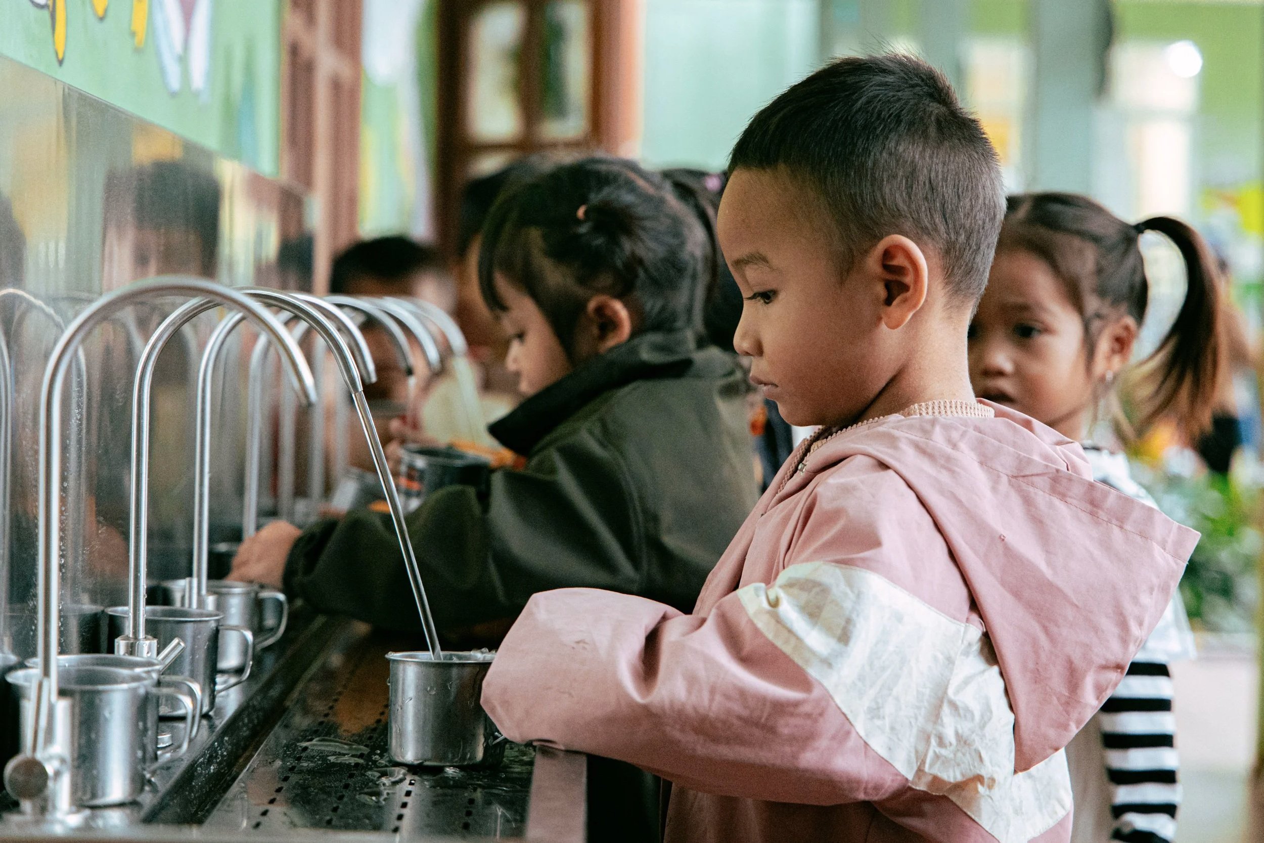 Children using a filtered water fountain in a school hallway.