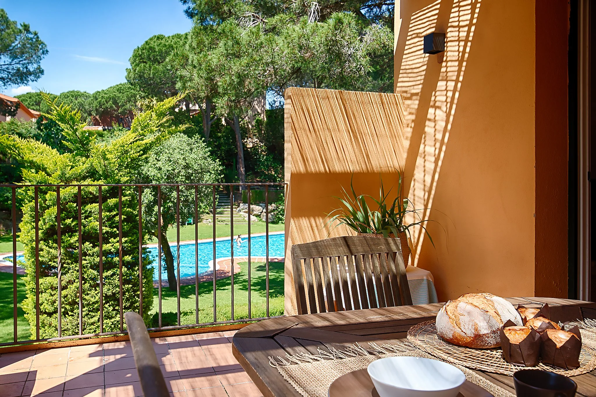Mediterranean terrace with great views of the swimming pool, bread on a basket, overlooking a garden with trees and a swimming pool on a sunny day. In Sant Feliu de Guixols In Costa Brava Spain