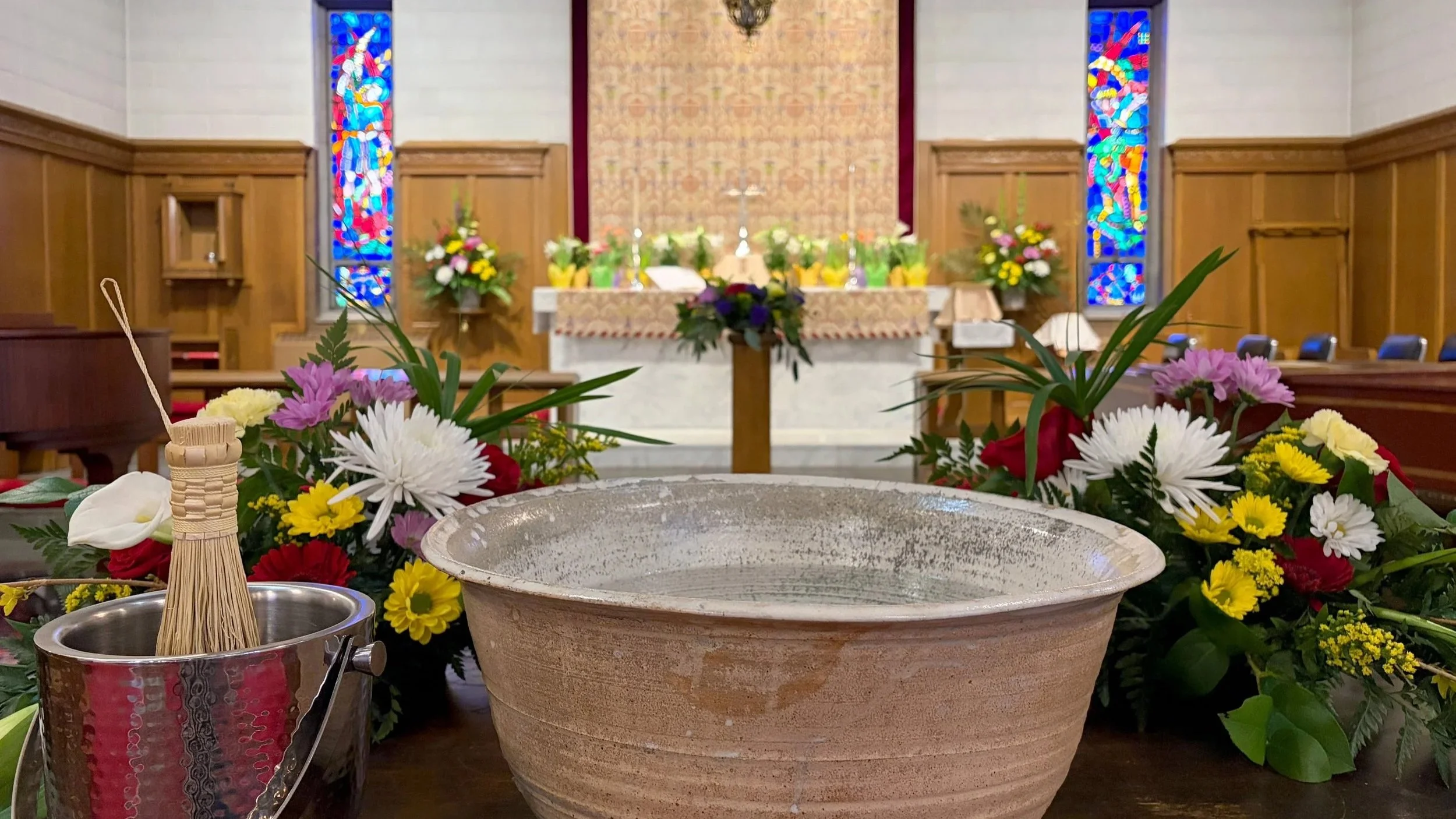 A church altar decorated with flowers, stained glass windows, and religious items, with a large empty bowl in the foreground.