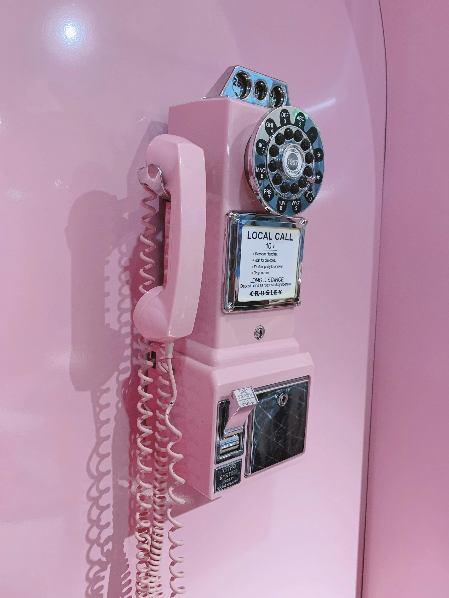 Pink vintage rotary payphone mounted on a pink wall.