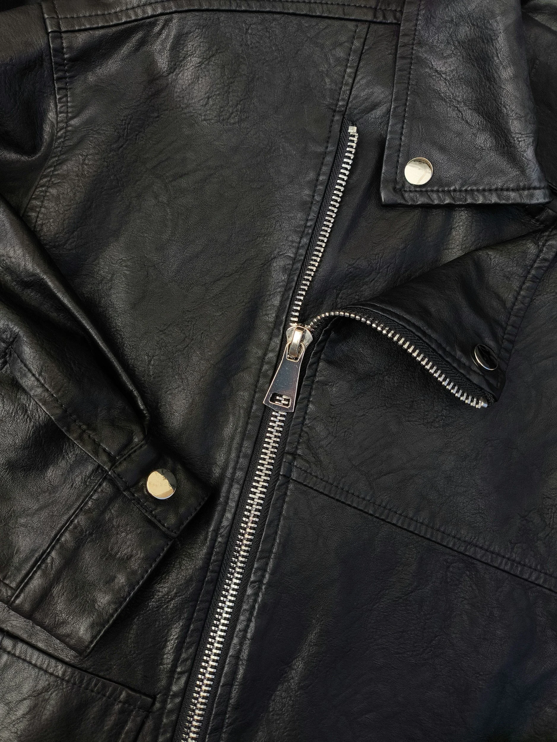 Close-up of a black leather jacket with a zipper and snap buttons.