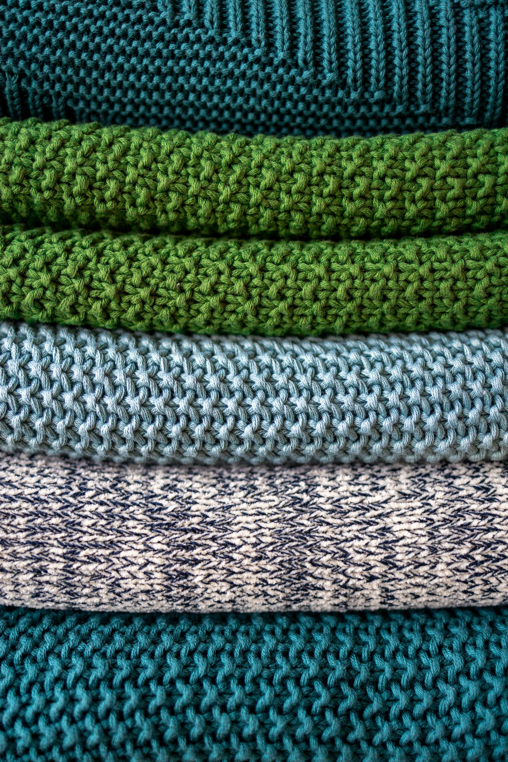 Stacked knitted sweaters in navy, green, light blue, gray, and teal colors.