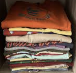 Stack of folded clothes, including T-shirts and shirts, placed on a shelf.