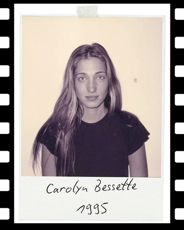 Black and white photo of a young woman with long wavy hair, wearing a black t-shirt, taped to a white background. Handwritten text below the photo says "Carolyn Bessette 1995."