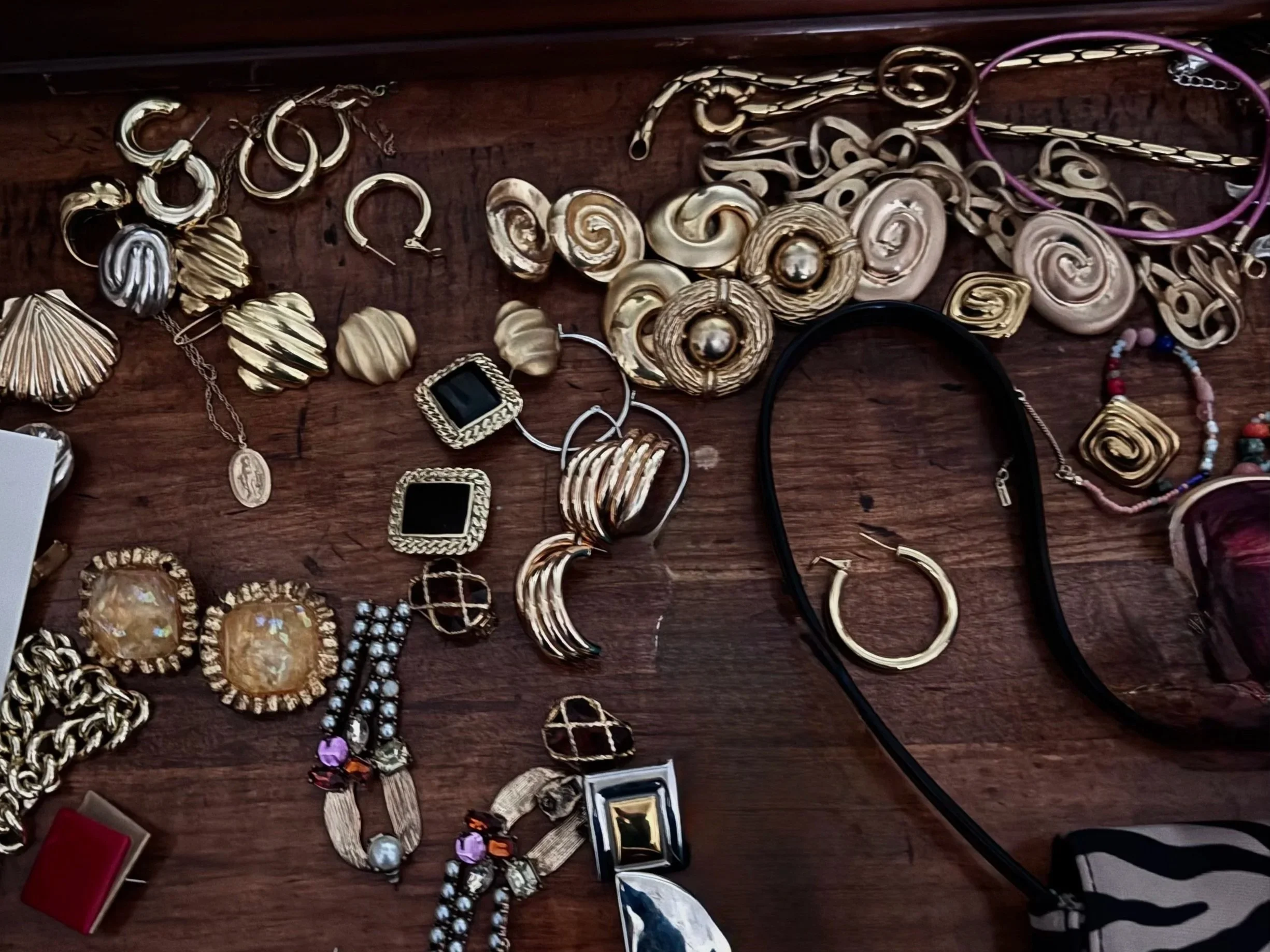 Various gold and silver jewelry pieces including earrings, necklaces, bracelets, and rings displayed on a wooden surface.