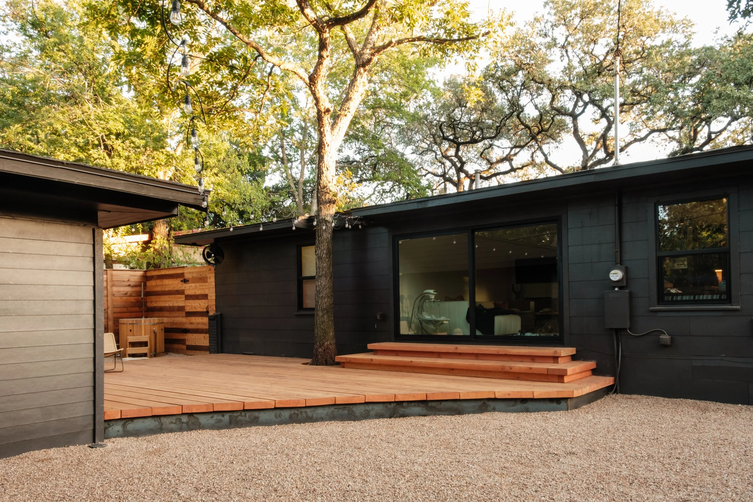 Real wood deck connected to a modern home with outdoor lighting and gravel ground cover.