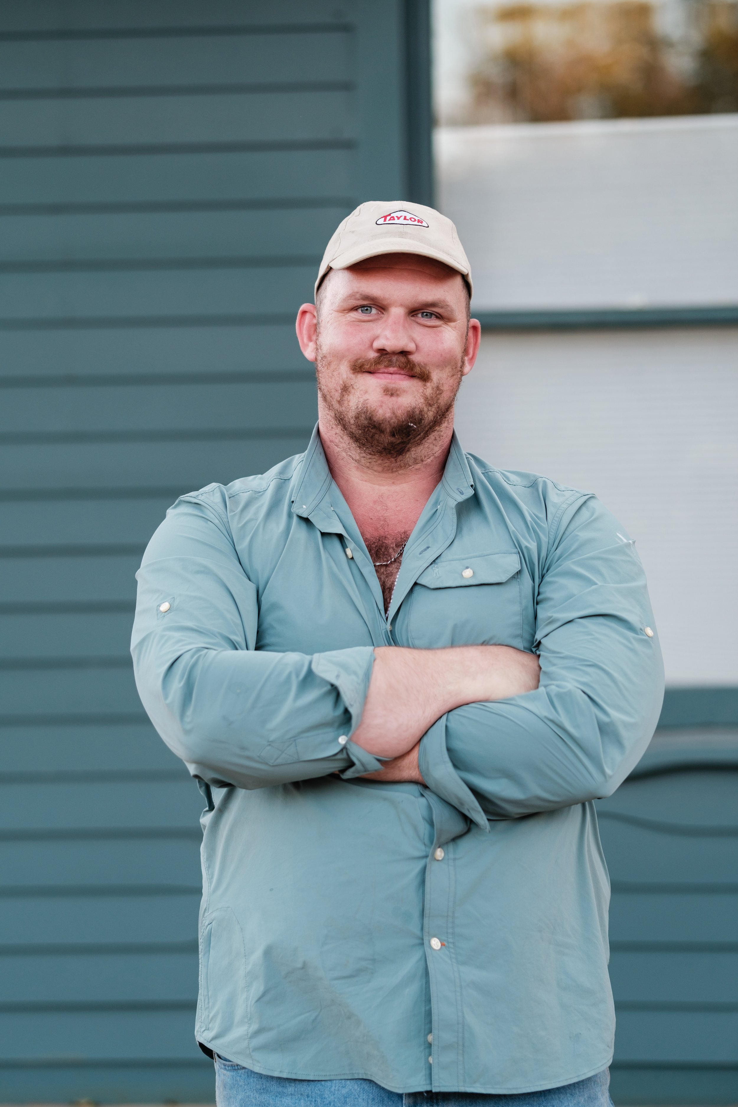 A person using a handheld angle grinder on a piece of wood outdoors, wearing gloves and red shorts.
